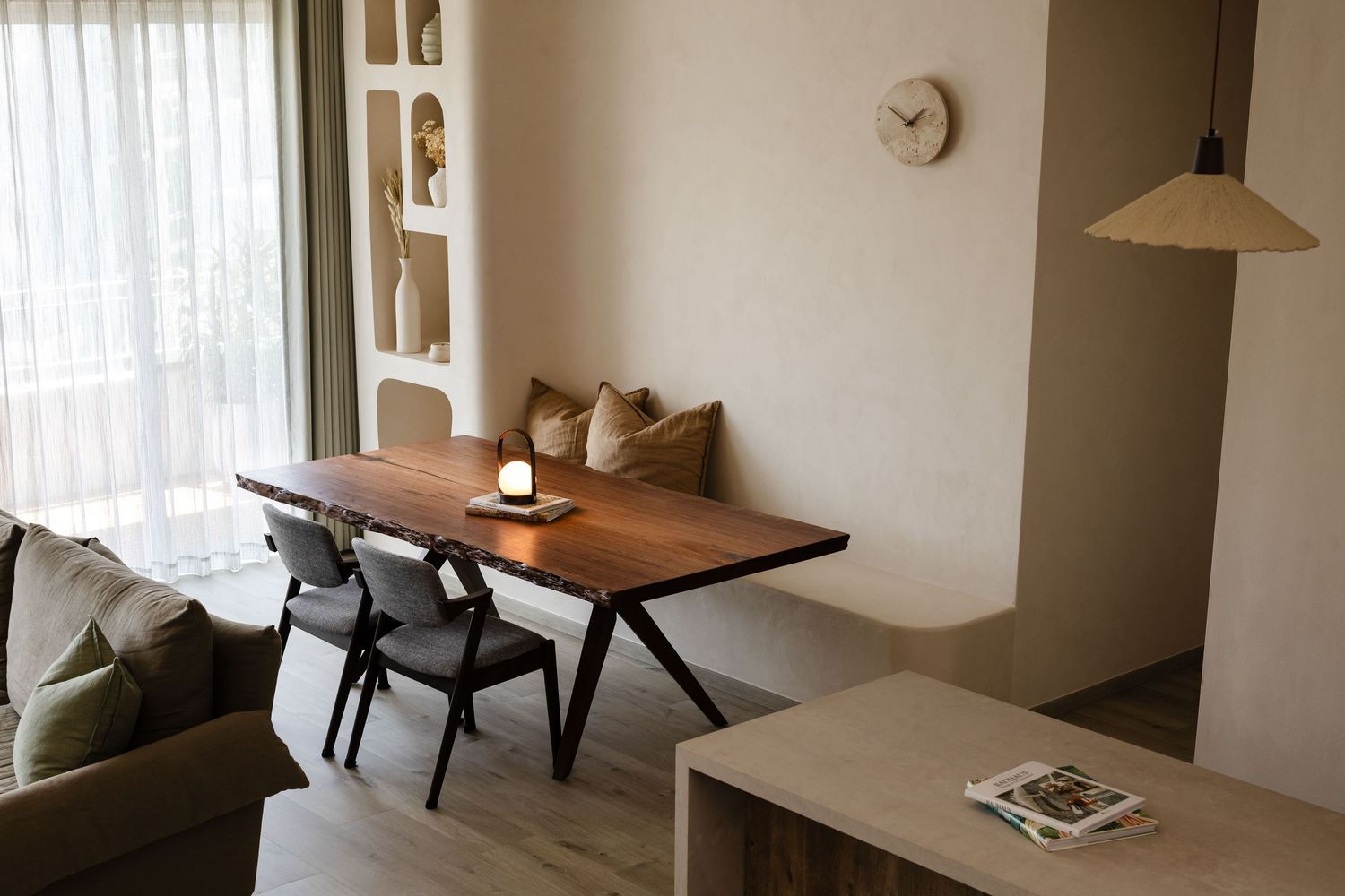 A minimalist apartment living room features white walls, hardwood floors, and modern furniture in neutral tones.