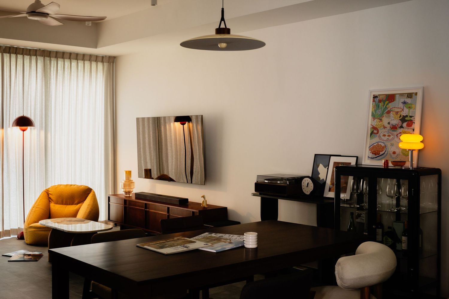 Modern apartment interior showing living spaces with stylish black and orange furnishings, tables and pendant lighting.