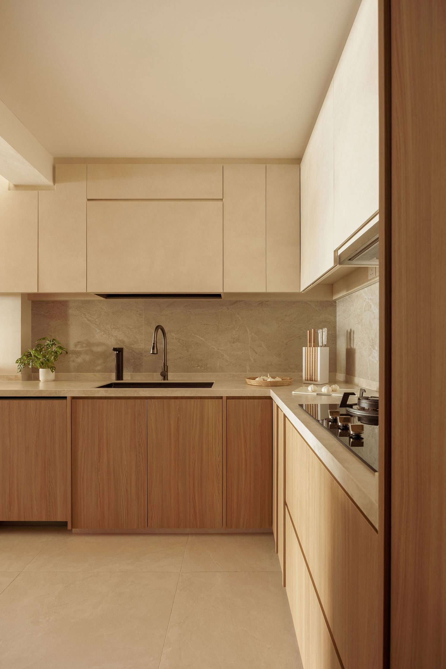 Modern minimalist kitchen with warm wood lower cabinets, cream upper cabinets, marble backsplash, black faucet, and built-in cooktop.