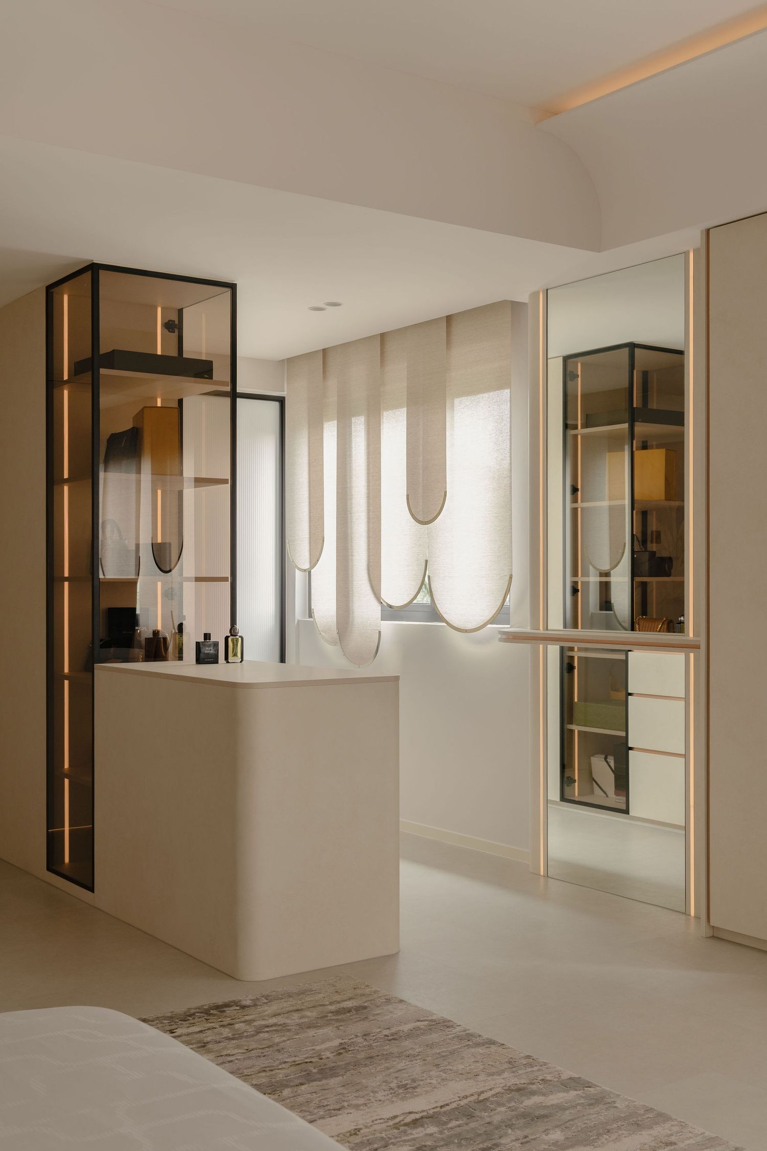 Modern minimalist bedroom with beige tones, black-framed glass shelving, vanity area, and sheer curtains.