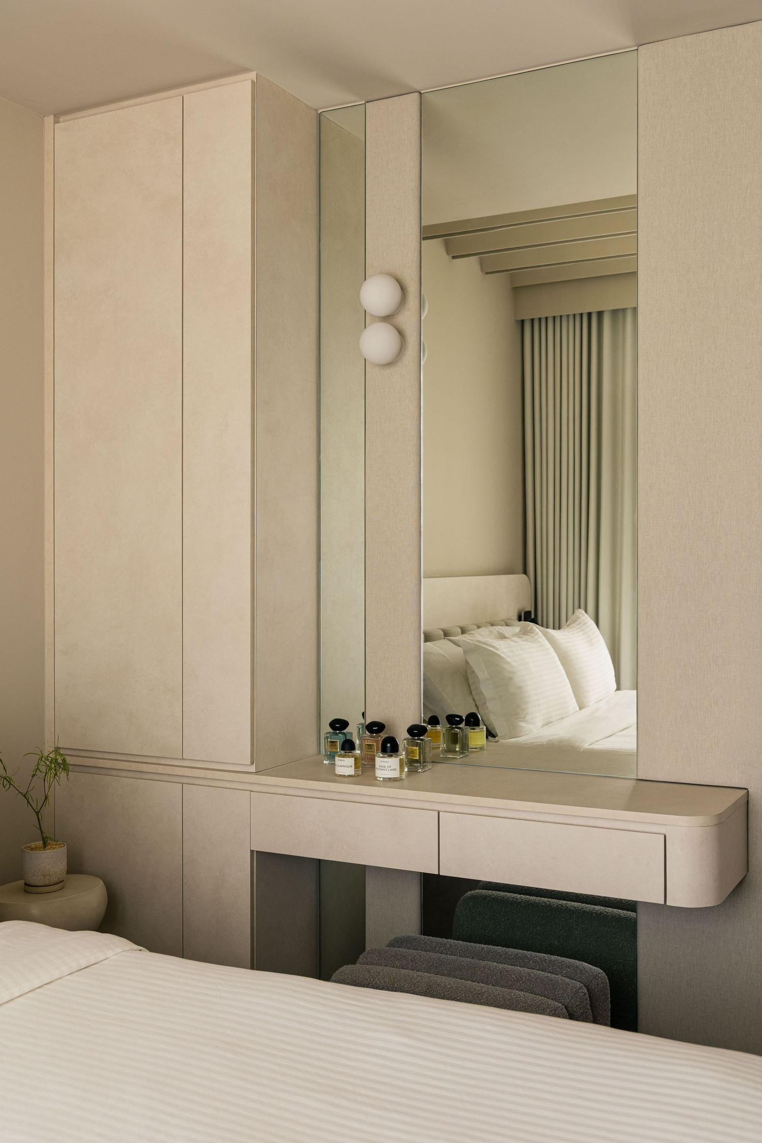 Minimalist hotel room vanity with large mirror, perfume bottles, and built-in wardrobe in neutral tones.