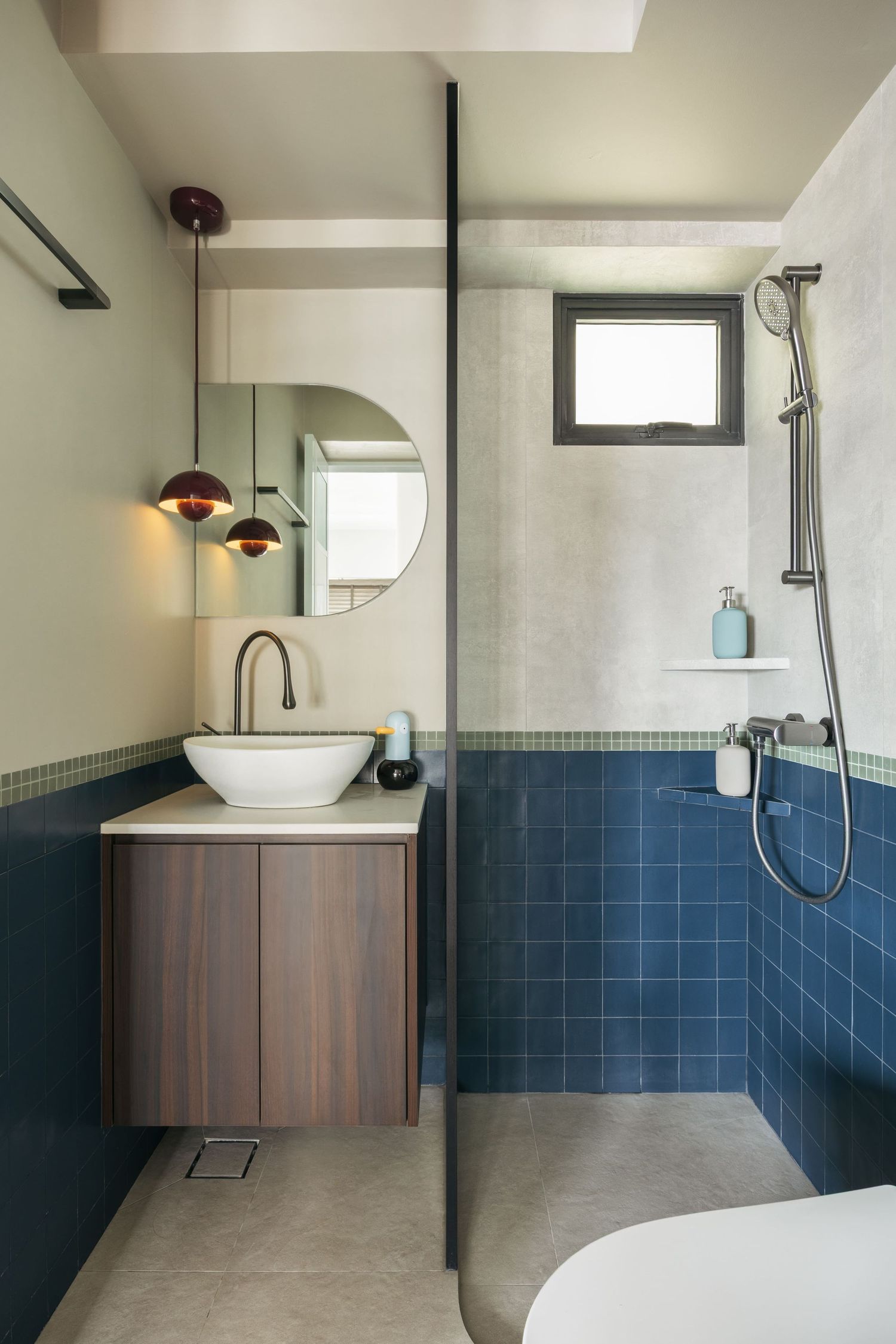 Modern bathroom with blue tiles, wooden vanity, vessel sink, round mirror, and glass shower partition.