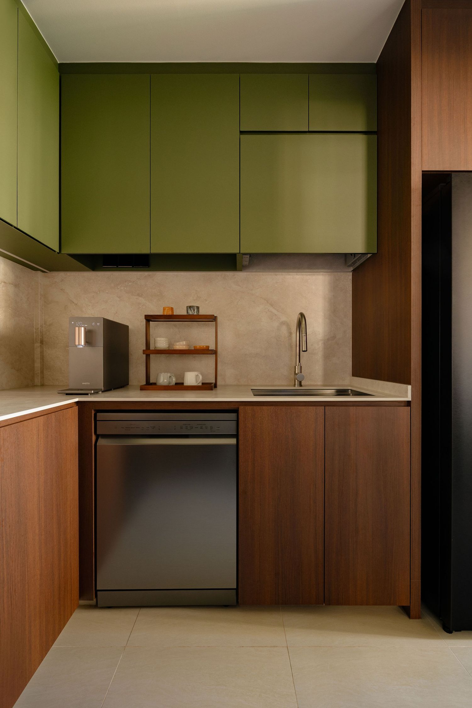 Modern L-shaped kitchen with olive green upper cabinets, walnut wood lower cabinets, stainless steel dishwasher and beige stone backsplash.