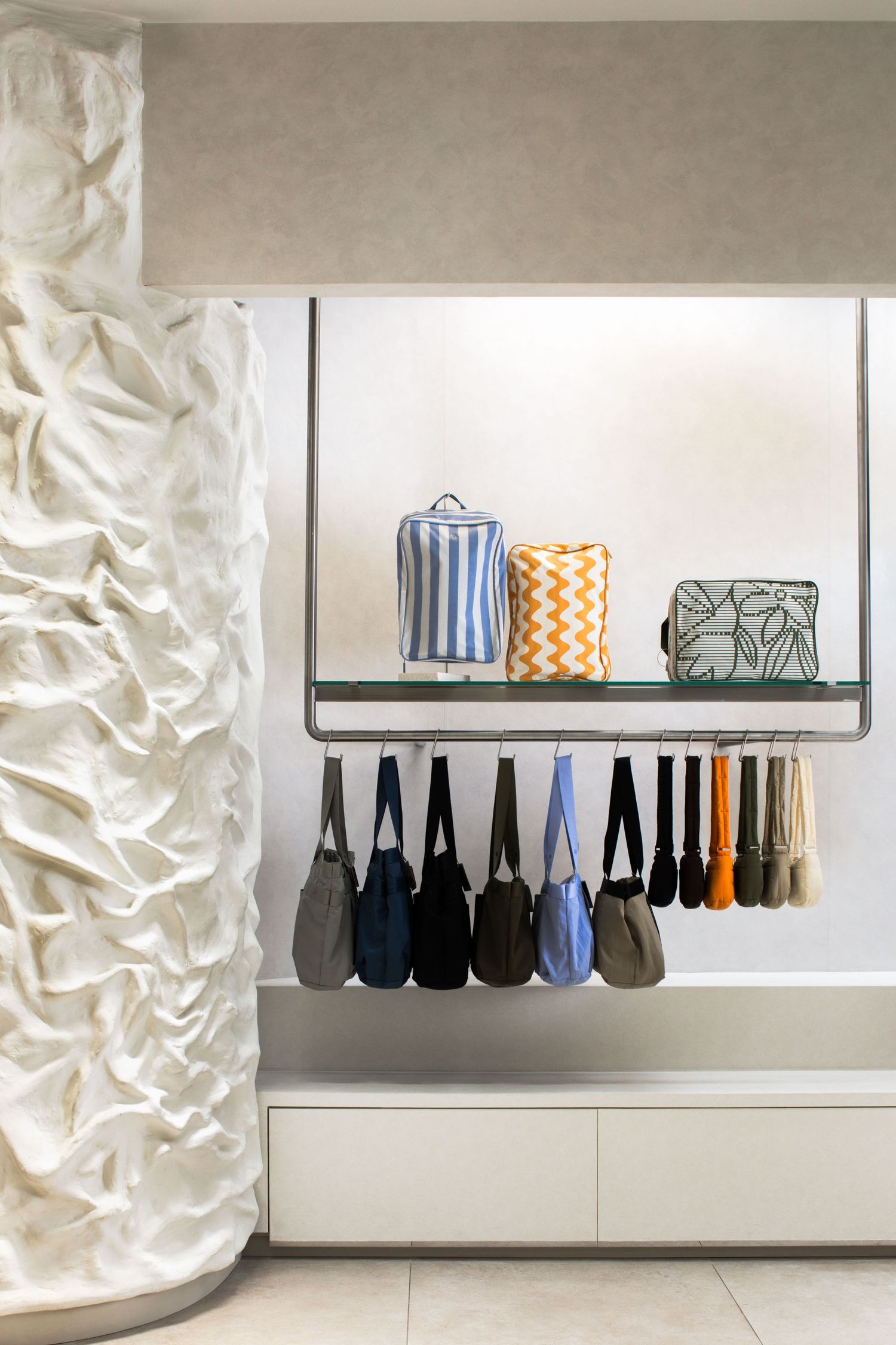 Modern closet organization with hanging purses and decorative storage containers on a shelf against white wall.