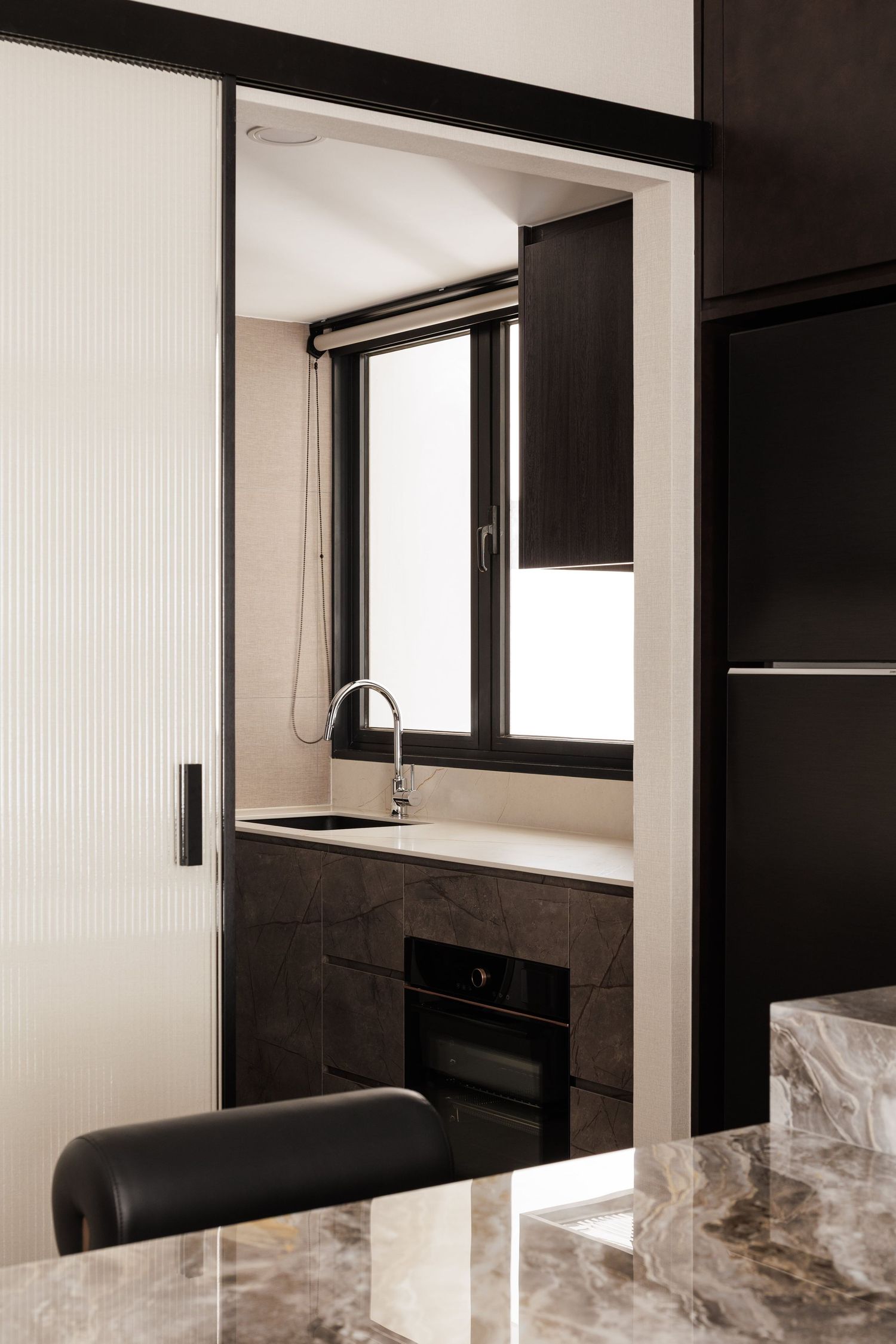 Modern minimalist kitchen interior with black and white color scheme featuring sleek cabinetry and window lighting.