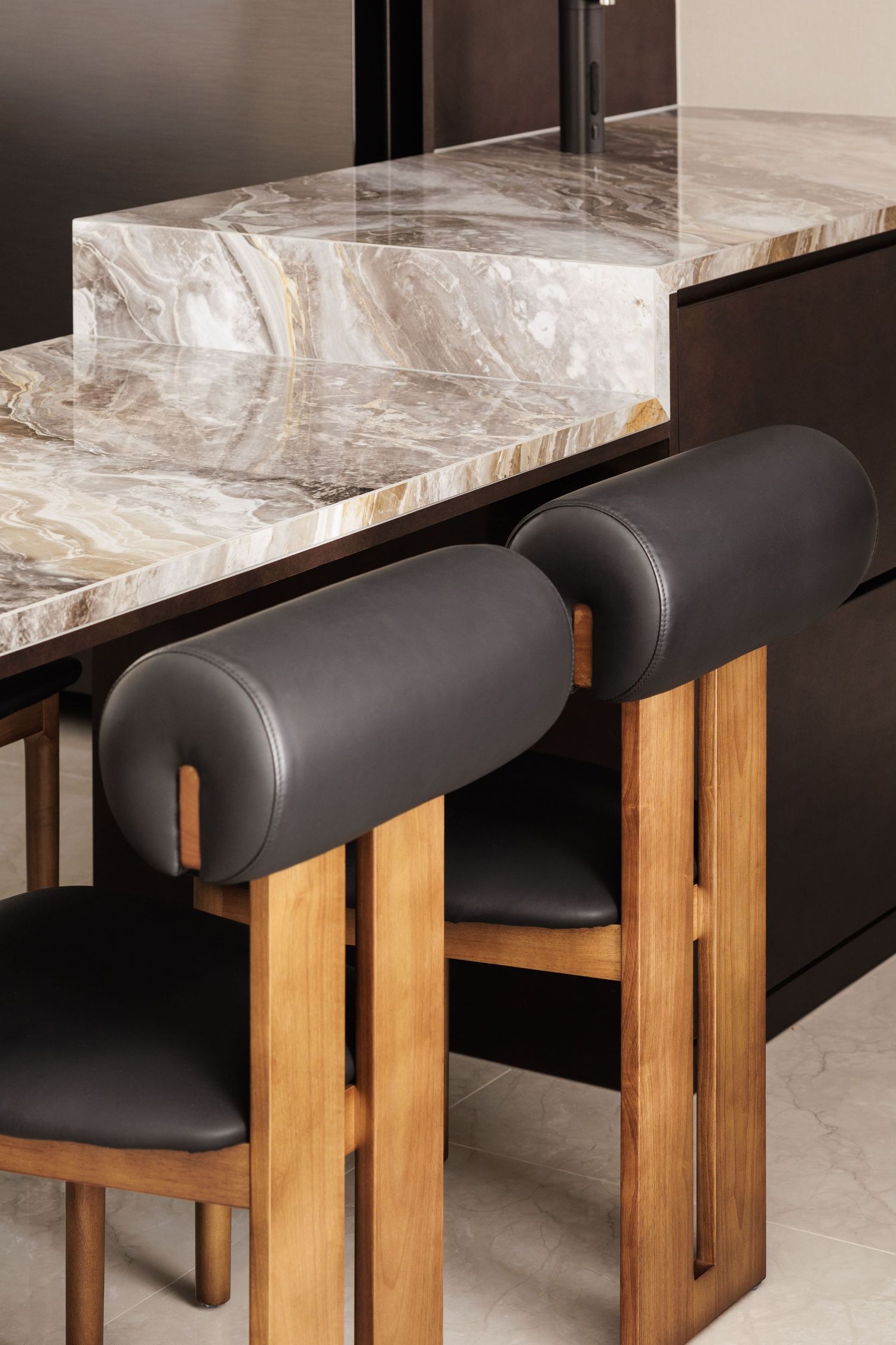 Modern dining setup with black leather chairs and marble table tops supported by wooden legs in a minimalist design.
