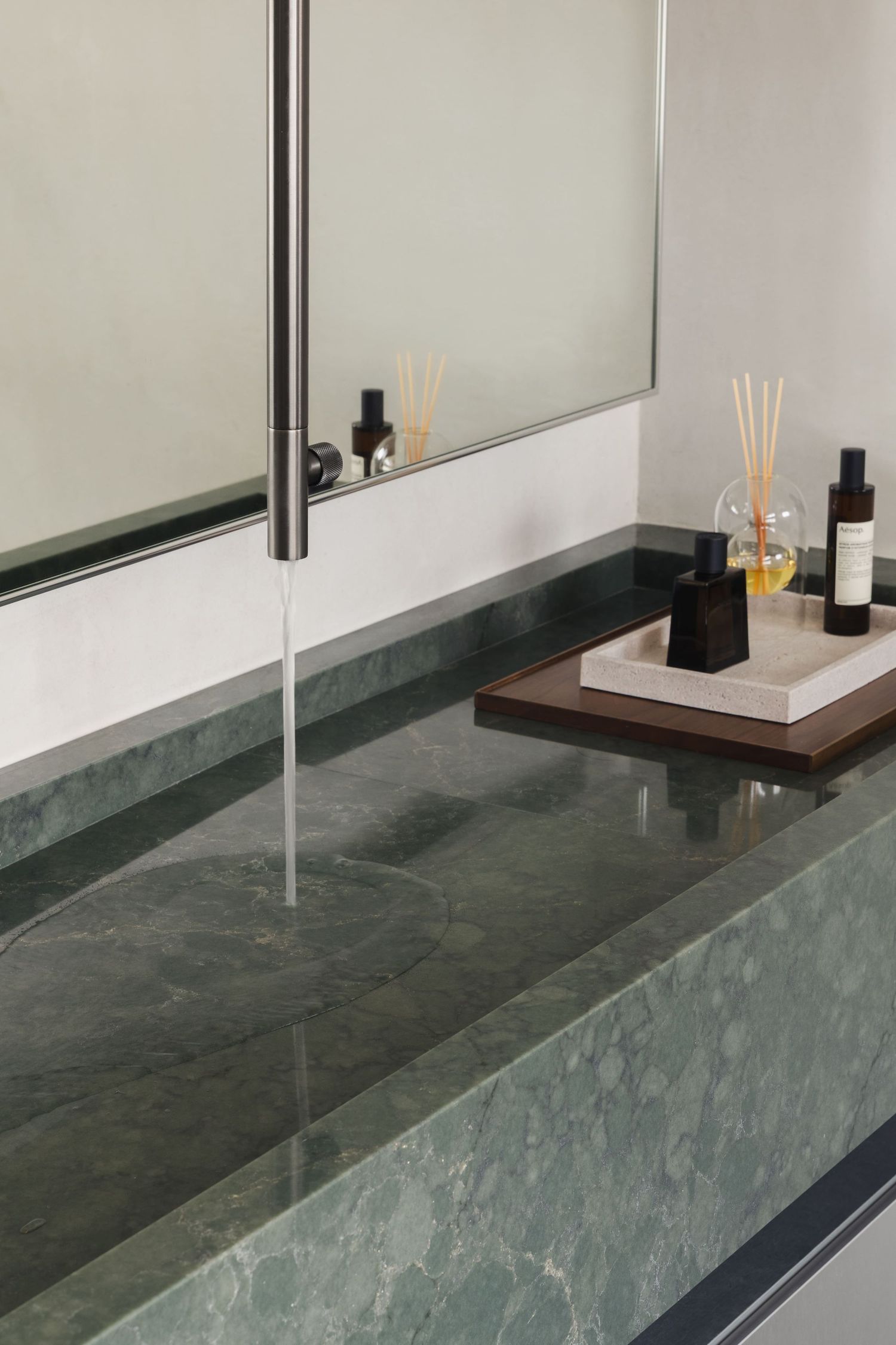 Elegant green marble bathroom vanity with sleek faucet, mirror, and luxury toiletries on a wooden tray.