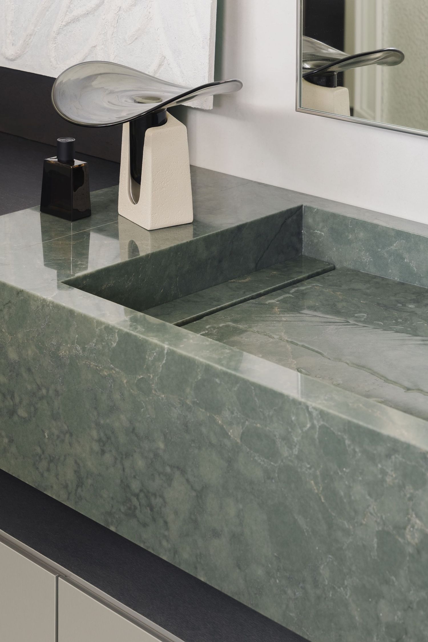 Elegant green marble bathroom sink with wall-mounted faucet, decorative vase, and mirror on a modern vanity countertop.