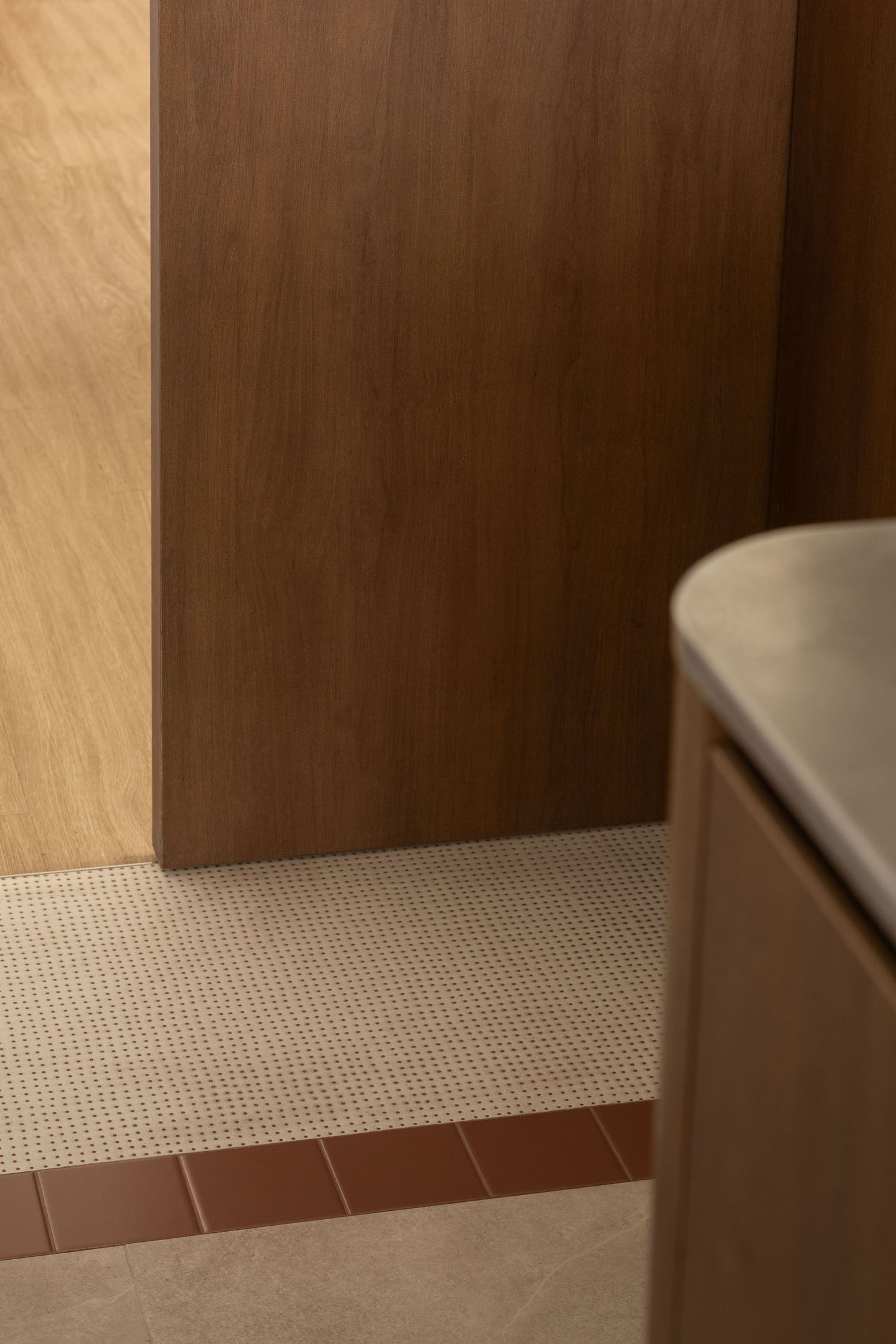A close-up view of a textured mosaic tile wall with a brown wooden panel above it.