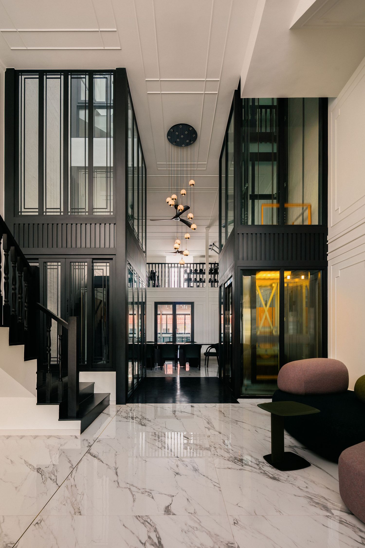 Double-height luxury foyer with white marble floors, black framed glass walls, a modern staircase, pendant chandelier and plush mauve lounge