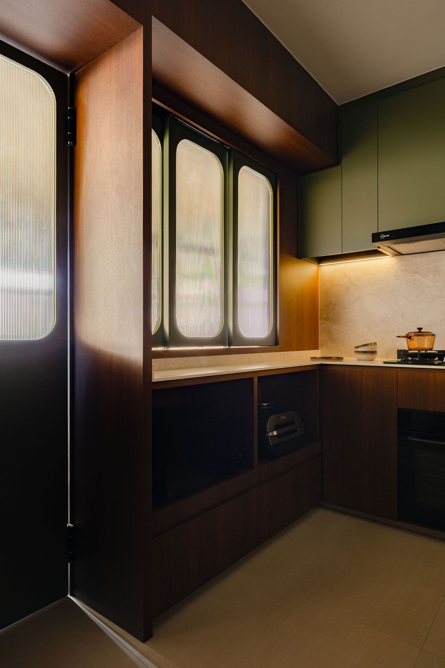 Modern kitchen corner with walnut wood cabinetry, sage green upper cabinets, fluted glass doors, warm under-cabinet lighting and a gas hob.