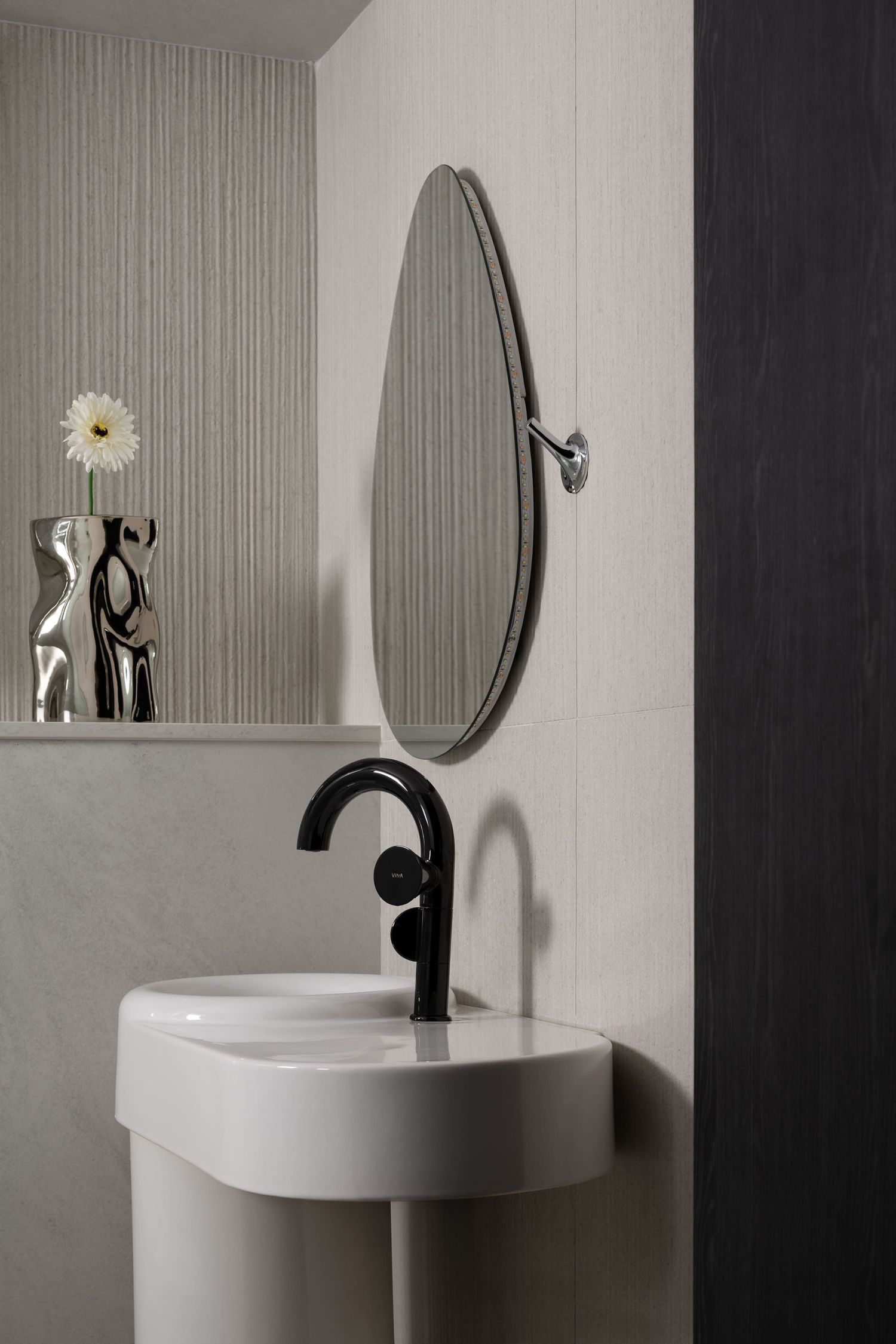 A modern minimalist bathroom features a white pedestal sink, round mirror, and black faucet against striped gray wallpaper.