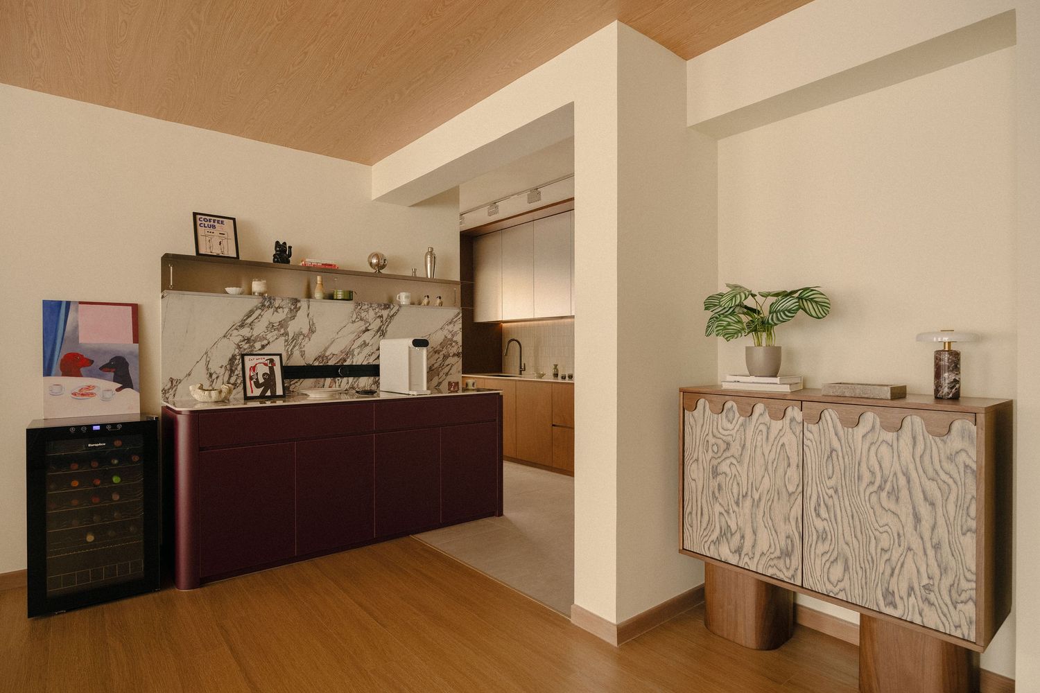 Modern home bar area with burgundy cabinetry, marble backsplash, wine fridge and patterned wooden sideboard beneath a wood-paneled ceiling.