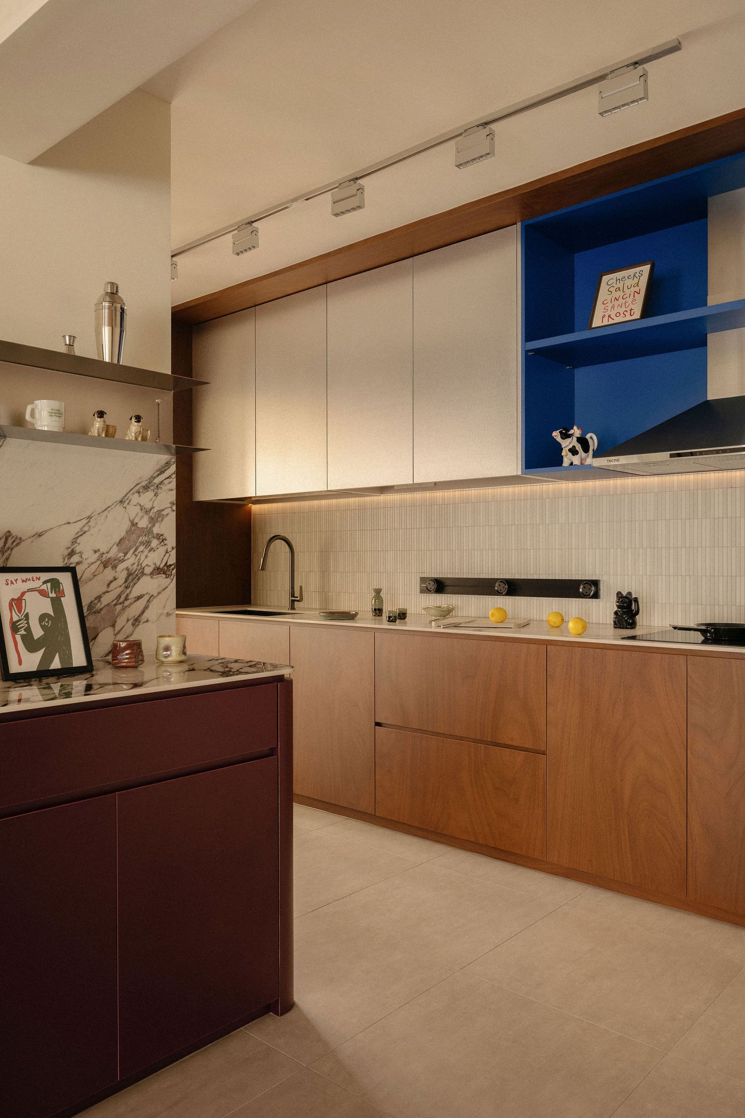 Modern kitchen with wood cabinetry, cobalt blue open shelving, marble accents, a burgundy island and warm under-cabinet lighting.