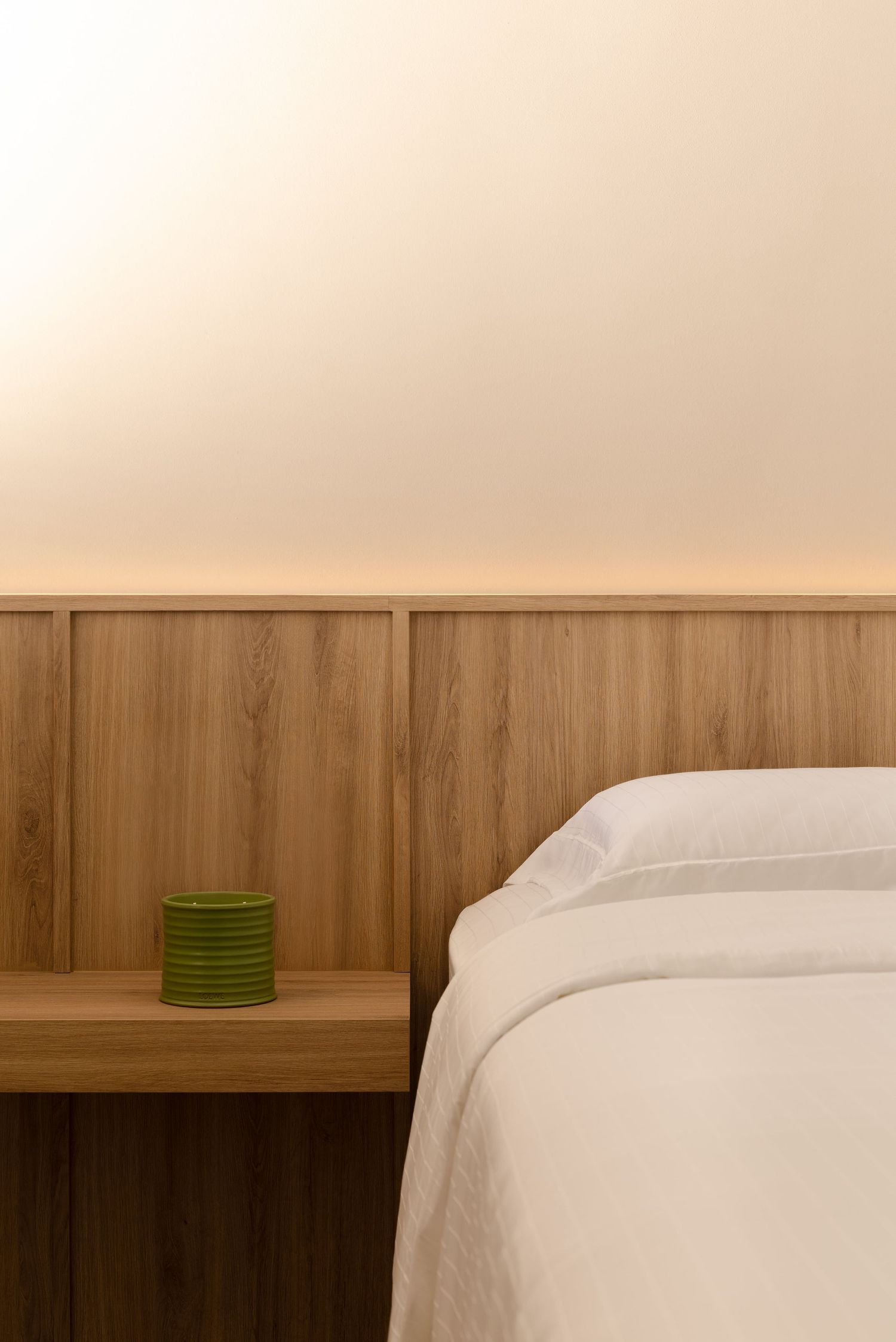 A minimalist bedroom interior with wooden paneling and a white bed against a neutral beige wall.