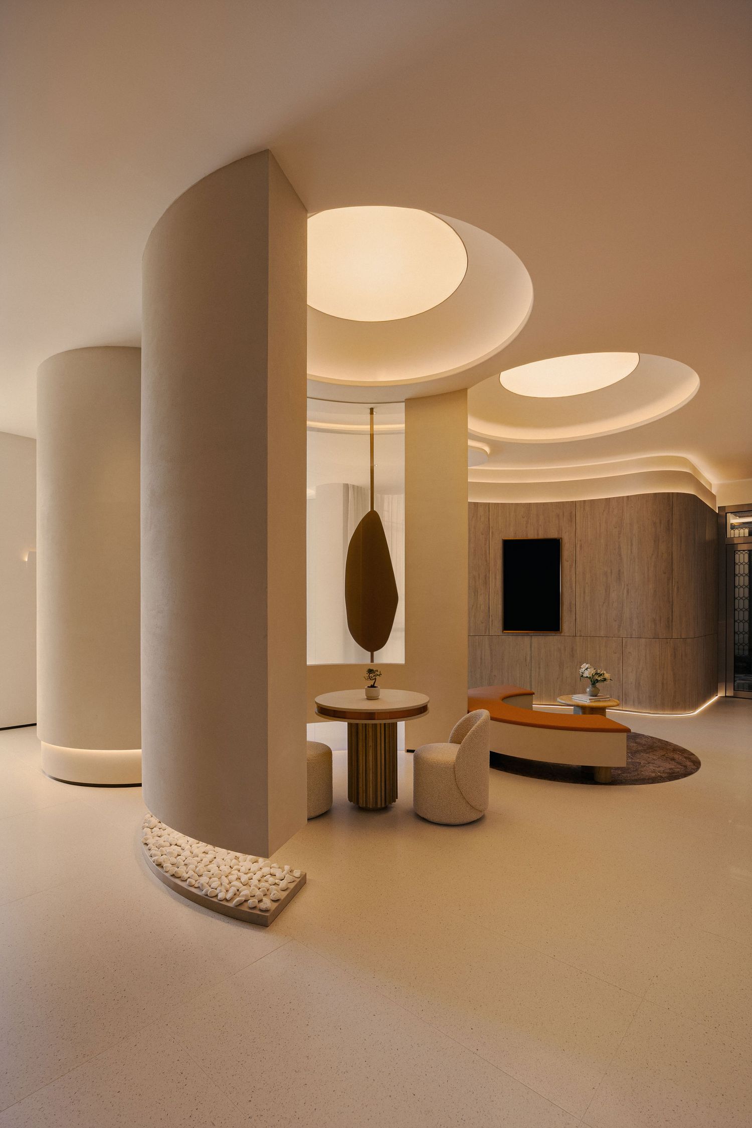 Modern luxury hotel lobby with curved cream columns, circular ceiling lights, and minimalist furniture in warm neutral tones.
