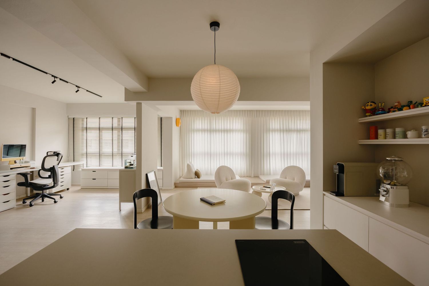 Modern open-plan living space with round dining table, pendant light, home office area, and neutral tones throughout.
