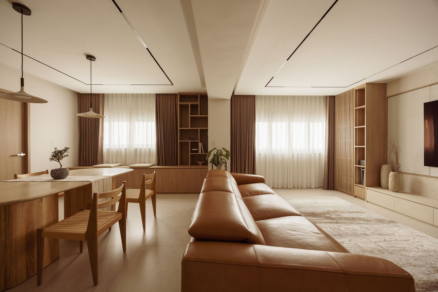 Modern living room with tan leather sofa, wooden built-in shelves, sheer curtains, and warm neutral tones.
