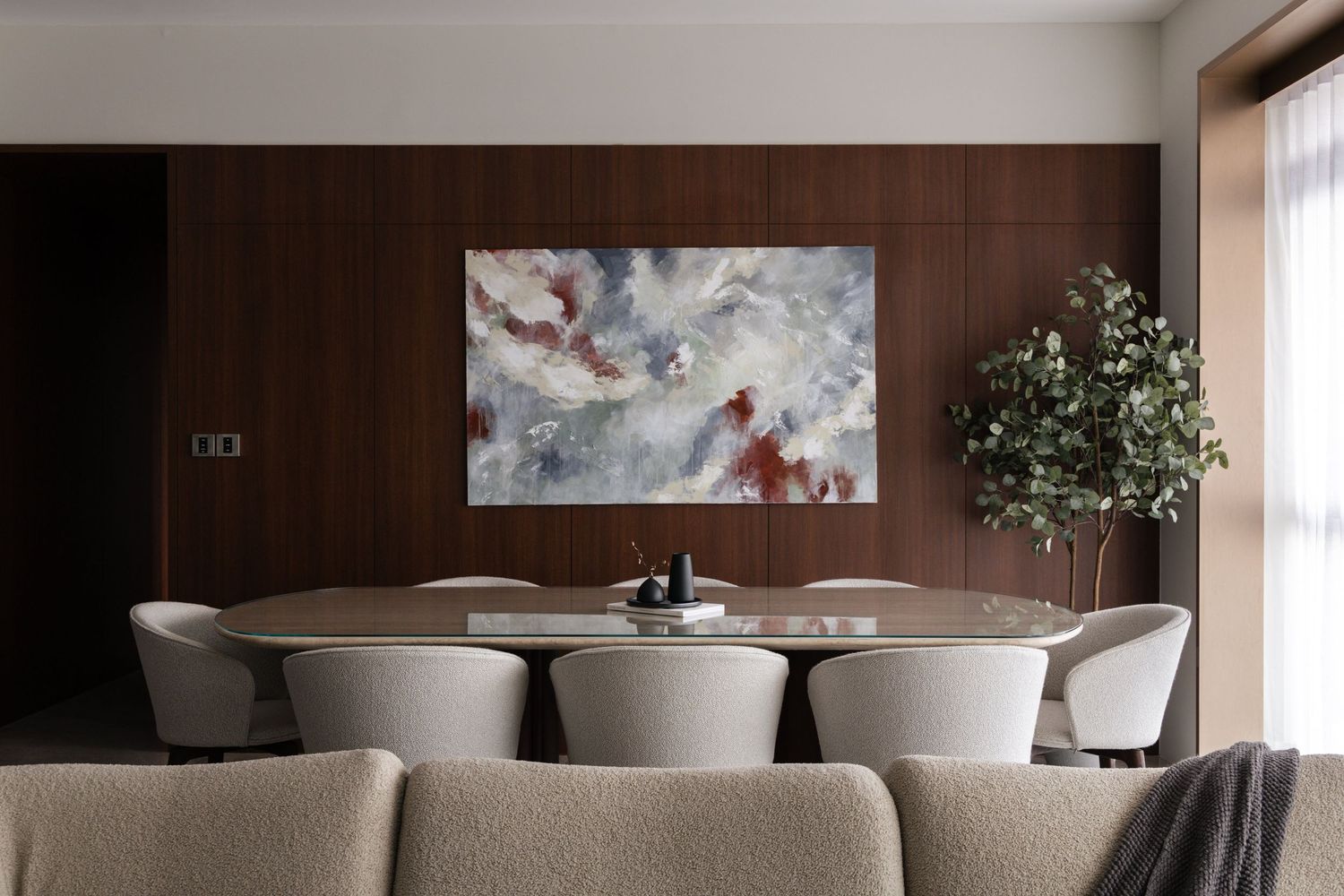 Elegant modern dining room with white chairs and dark wood paneling features contemporary artwork and natural lighting.