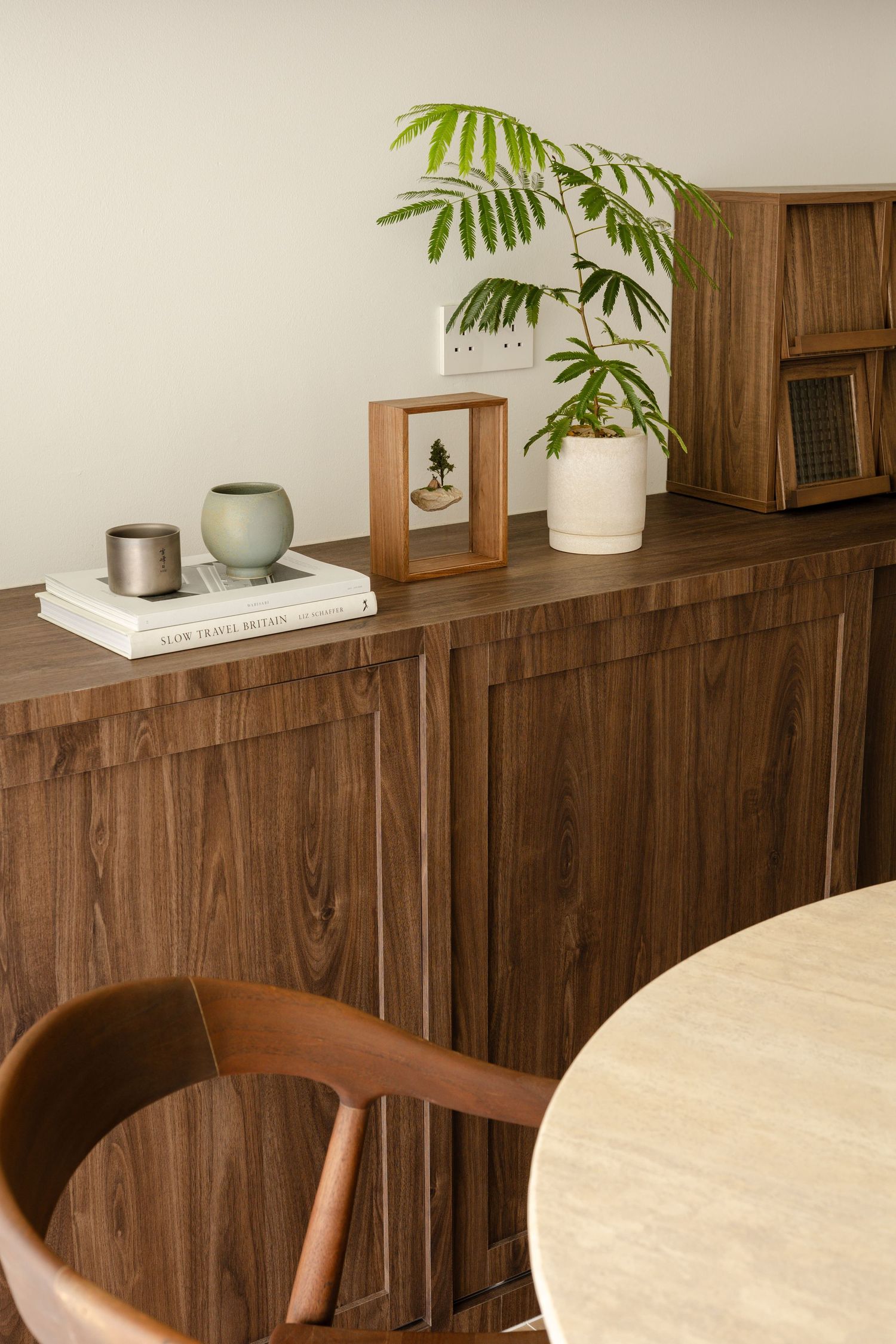 Modern minimalist dining area with wooden furniture, houseplant, and decorative items on a wooden cabinet.