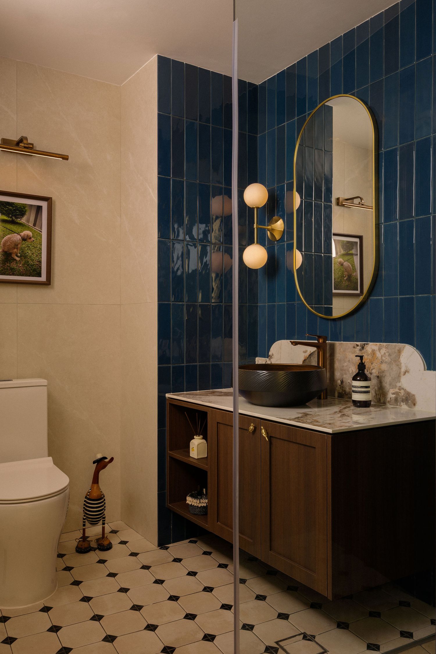 Stylish bathroom with deep blue glossy tile walls, an oval brass-framed mirror, wood vanity with vessel sink, and hexagonal patterned floor.