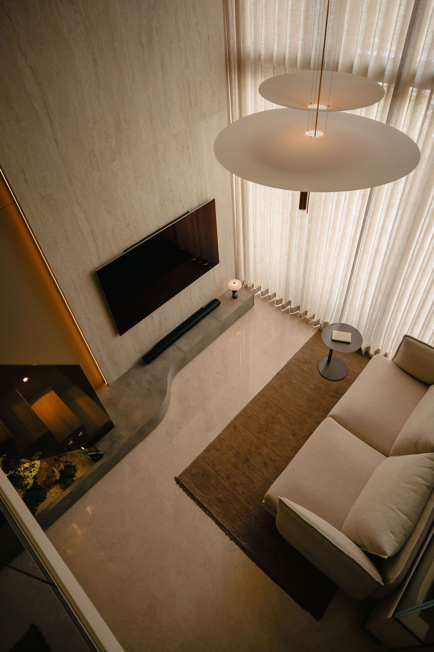 Overhead view of a modern living room with a cream sofa, wall-mounted TV, circular pendant lights, sheer curtains and a marble floor.