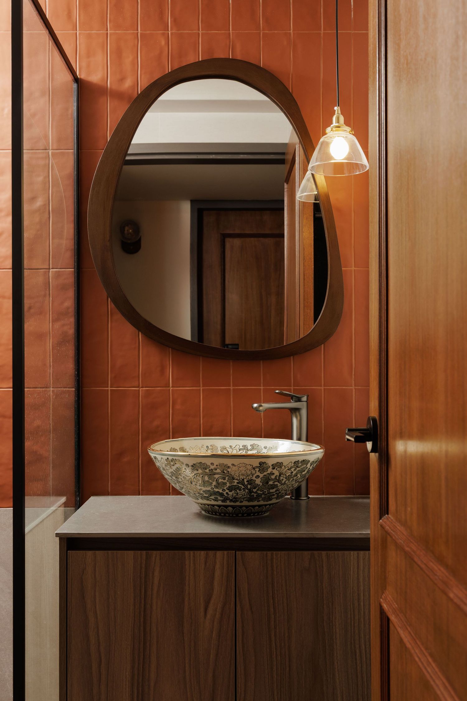 Modern bathroom interior with wooden walls, oval mirrors, and decorative vessel sink on dark countertop.