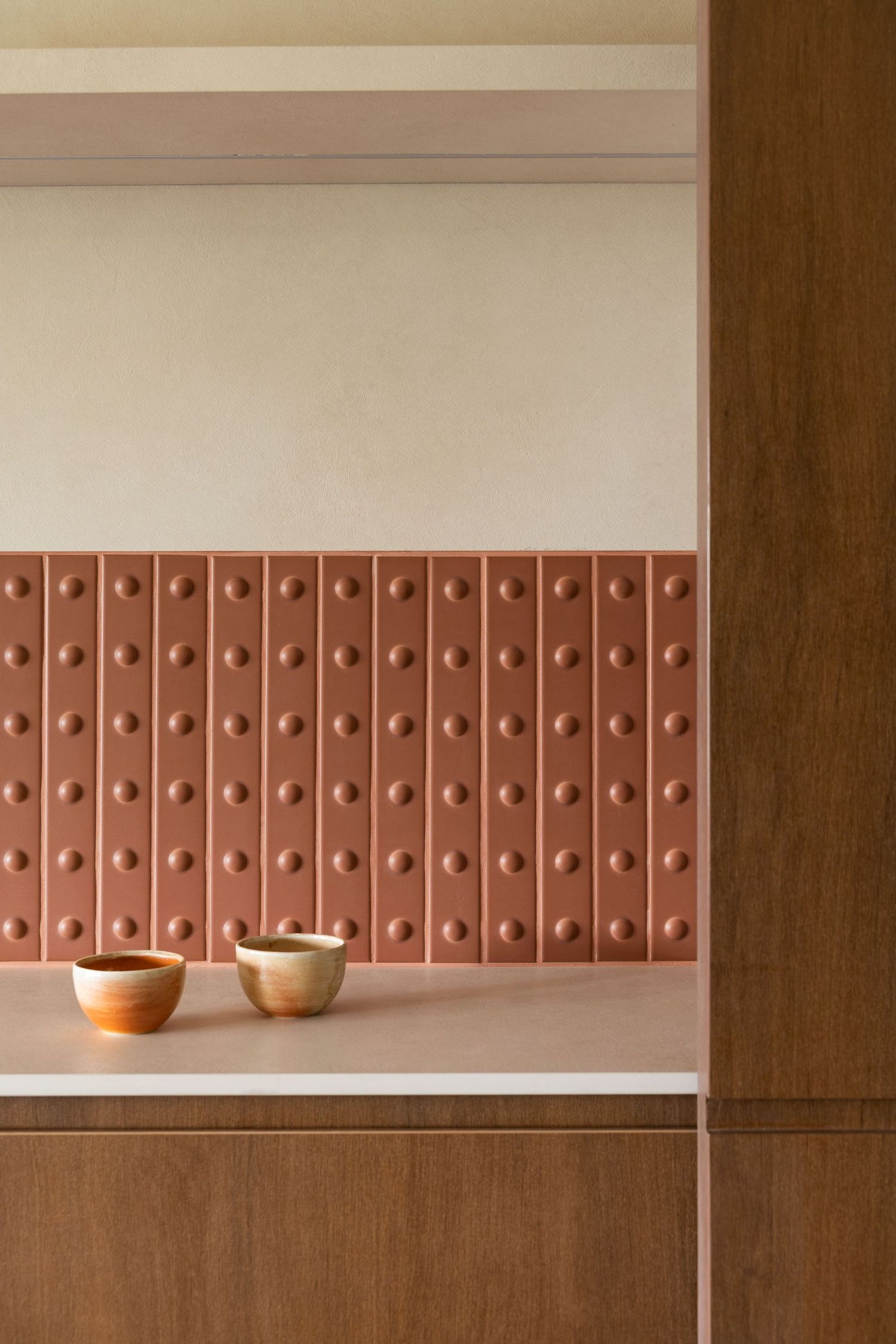 Minimalist architectural detail showing a row of pink tactile tiles against a beige wall with wooden paneling below.