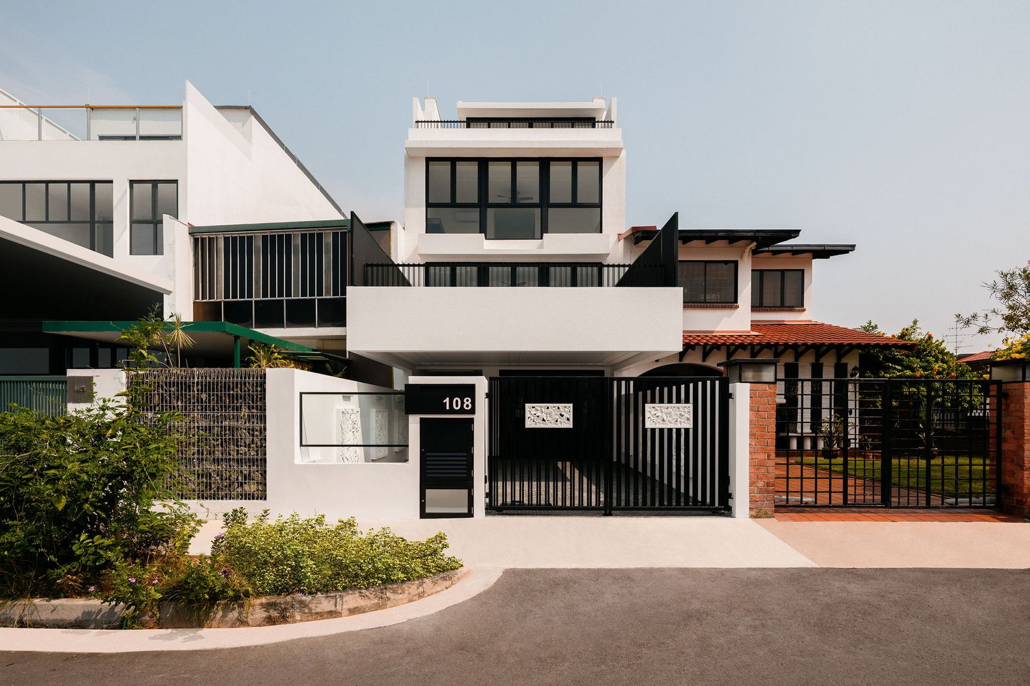 Modern multi-story white house with black gate, dark framed windows, landscaped front garden and driveway under a clear blue sky.