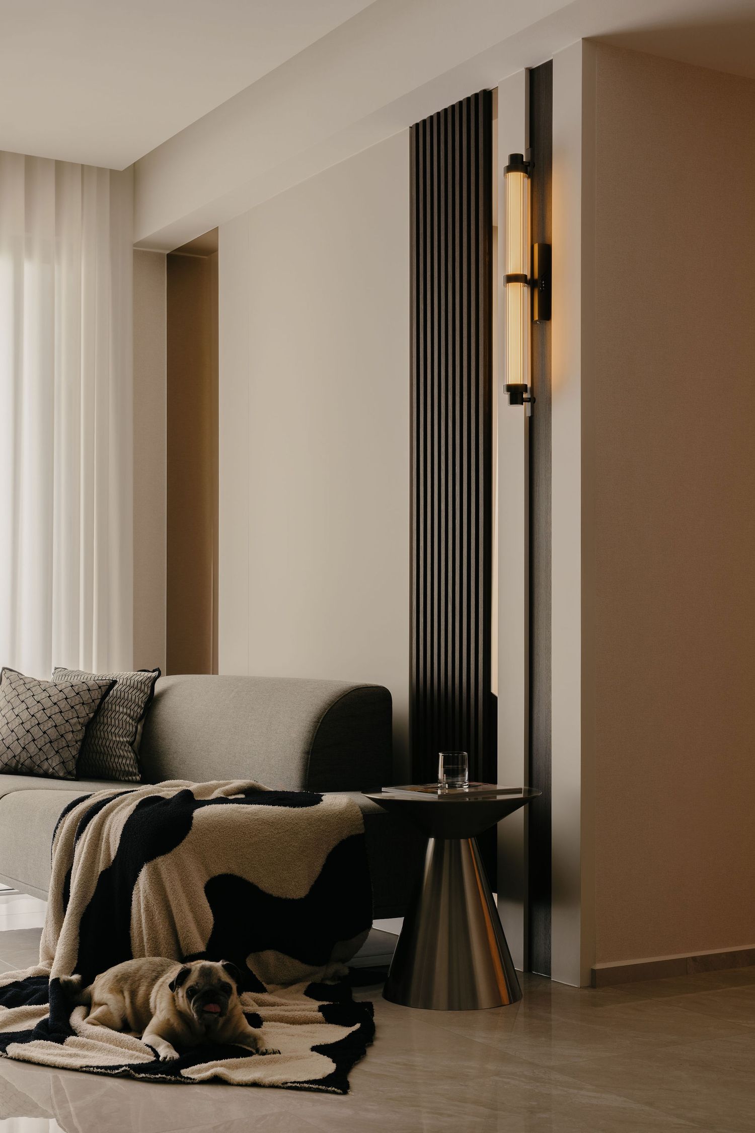 Modern minimalist living room with a gray sofa, black fluted panel, wall sconce, metal side table and a pug resting on a patterned throw.