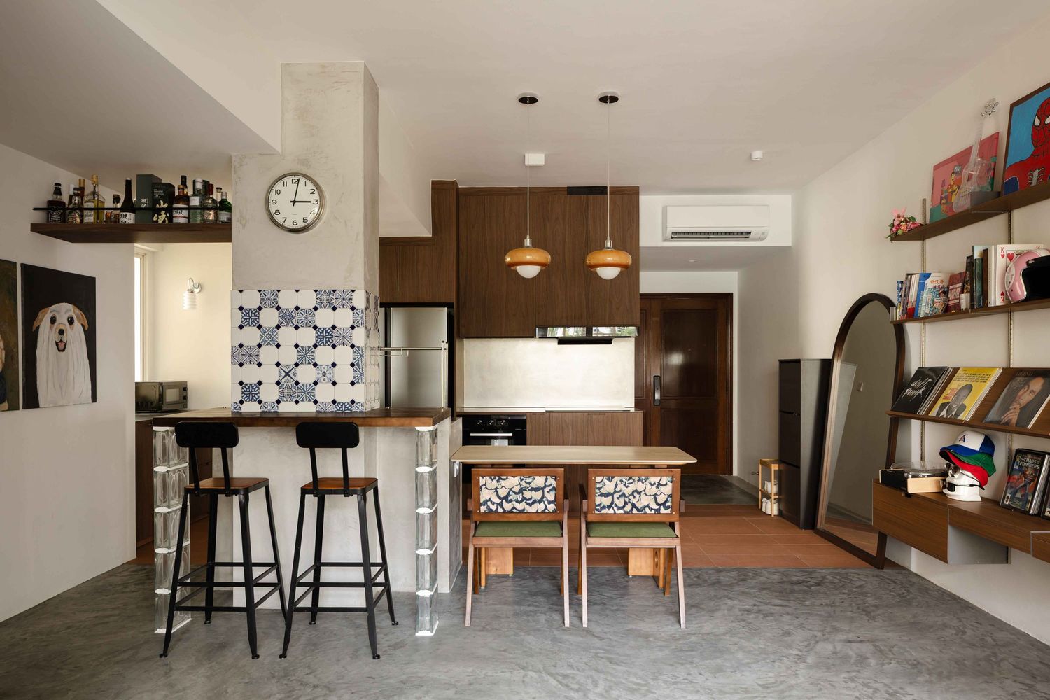 Modern open plan apartment with dining area, kitchen island, bar stools, and built-in bookshelves in neutral tones.