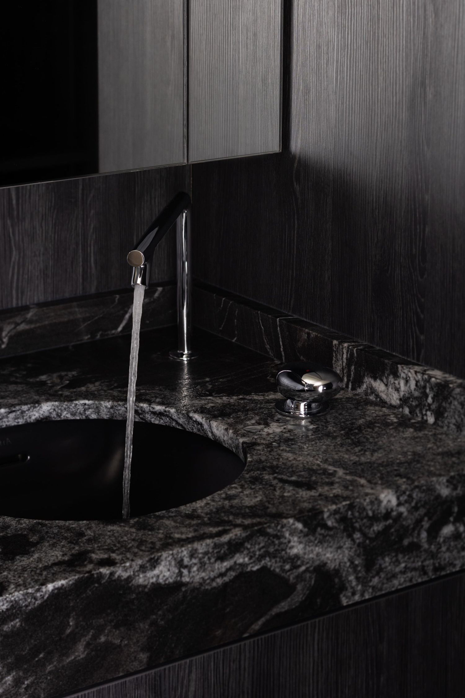 A modern black marble bathroom vanity with chrome faucet and dark wood paneled walls in dramatic lighting.