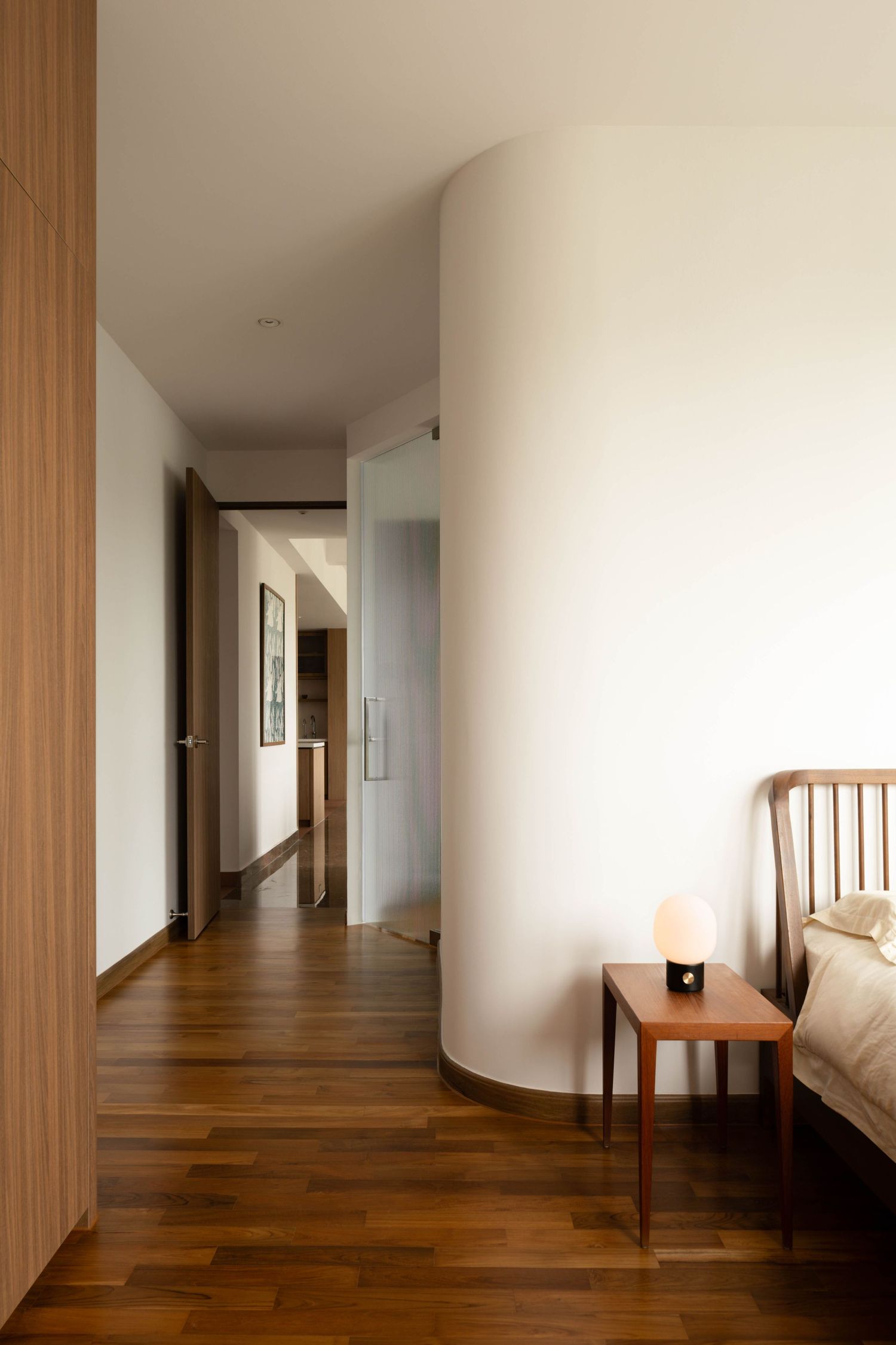 Modern minimalist hallway with hardwood flooring, white walls, and wooden accents leads to bright interior spaces.