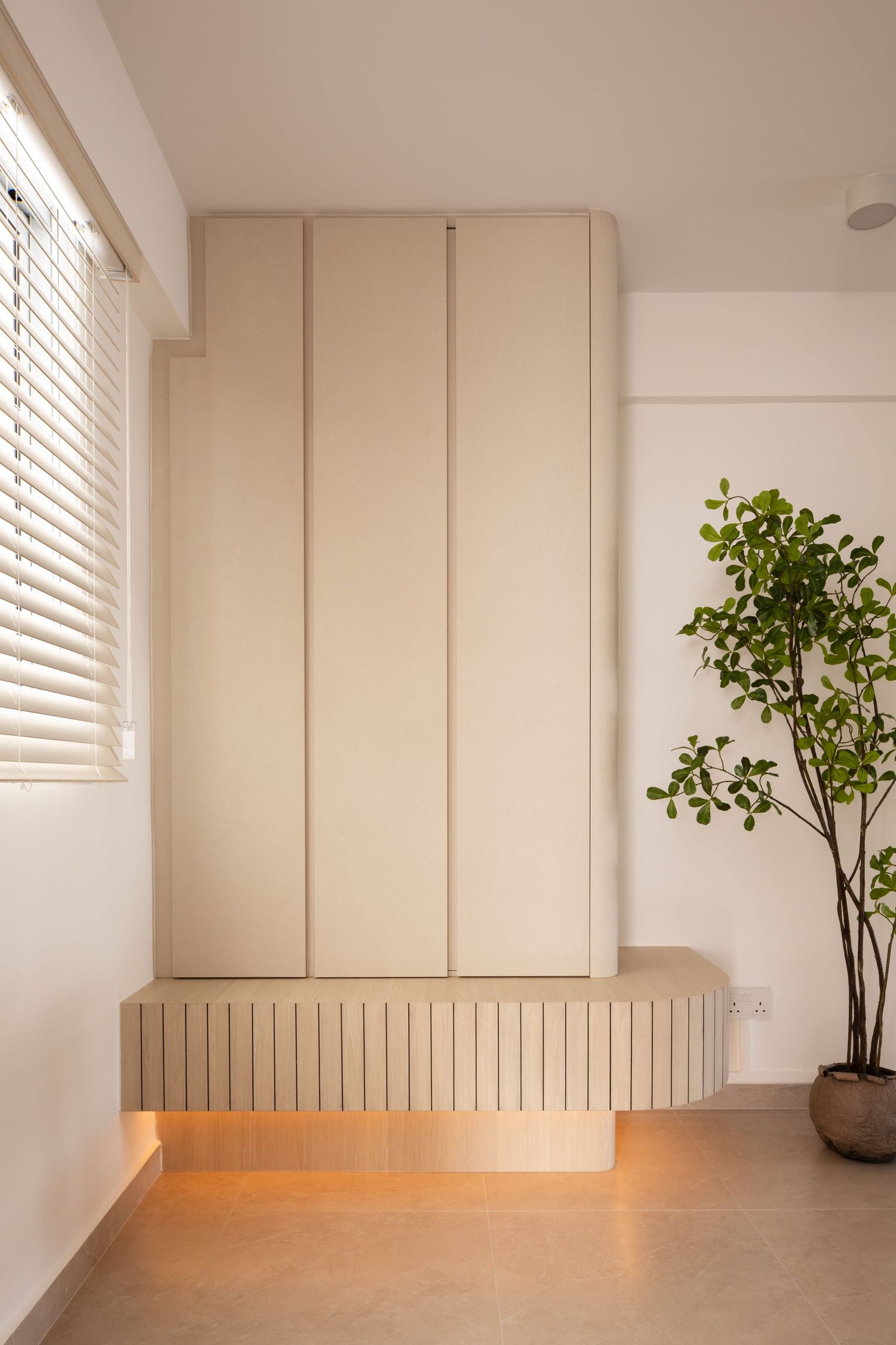 Minimalist white interior room with wooden flooring, venetian blinds, and a decorative green plant in a modern vase.