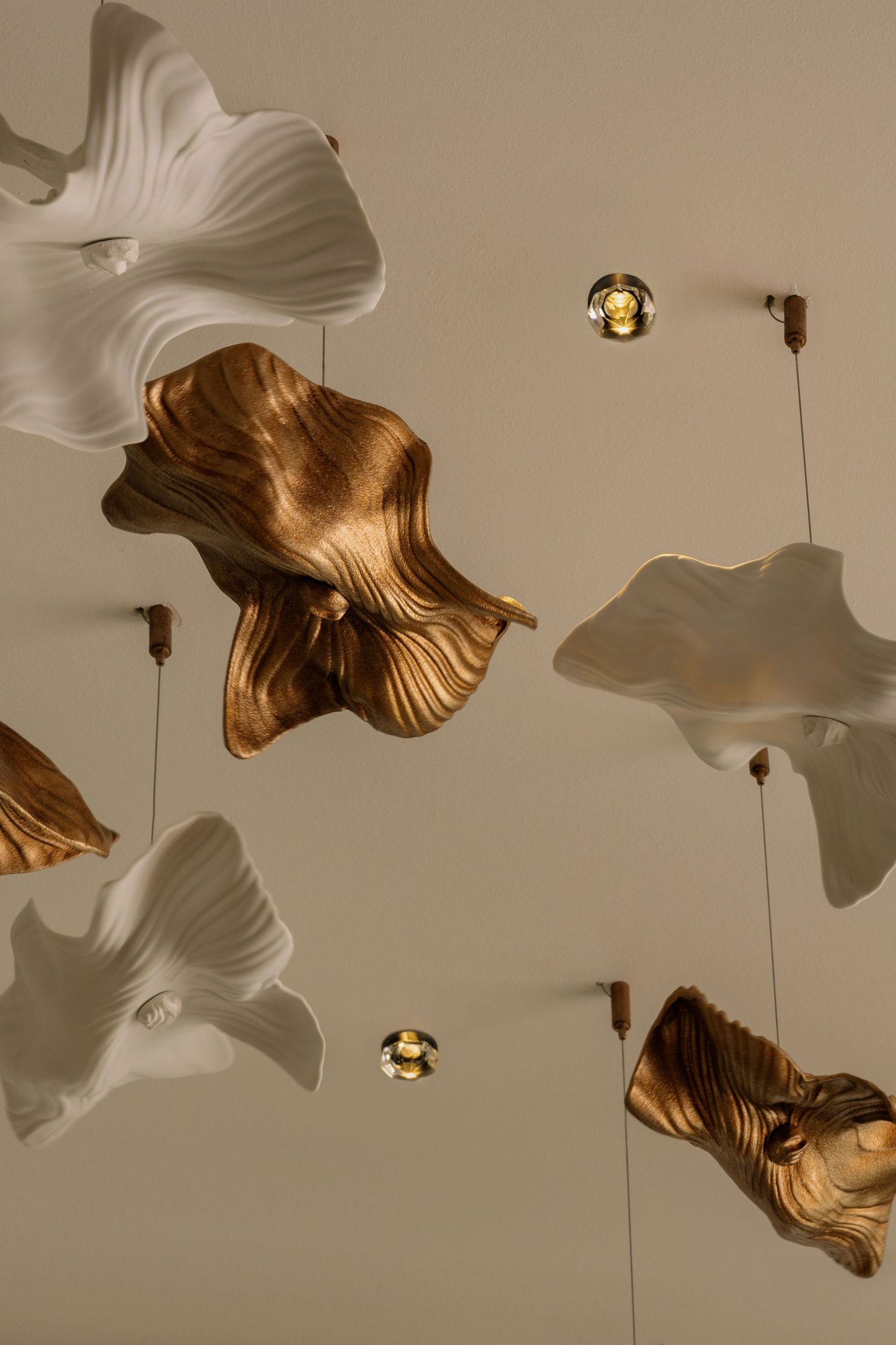 Elegant ceiling installation featuring sculptural white and bronze wavy flower-shaped pendants with small gold spotlights.