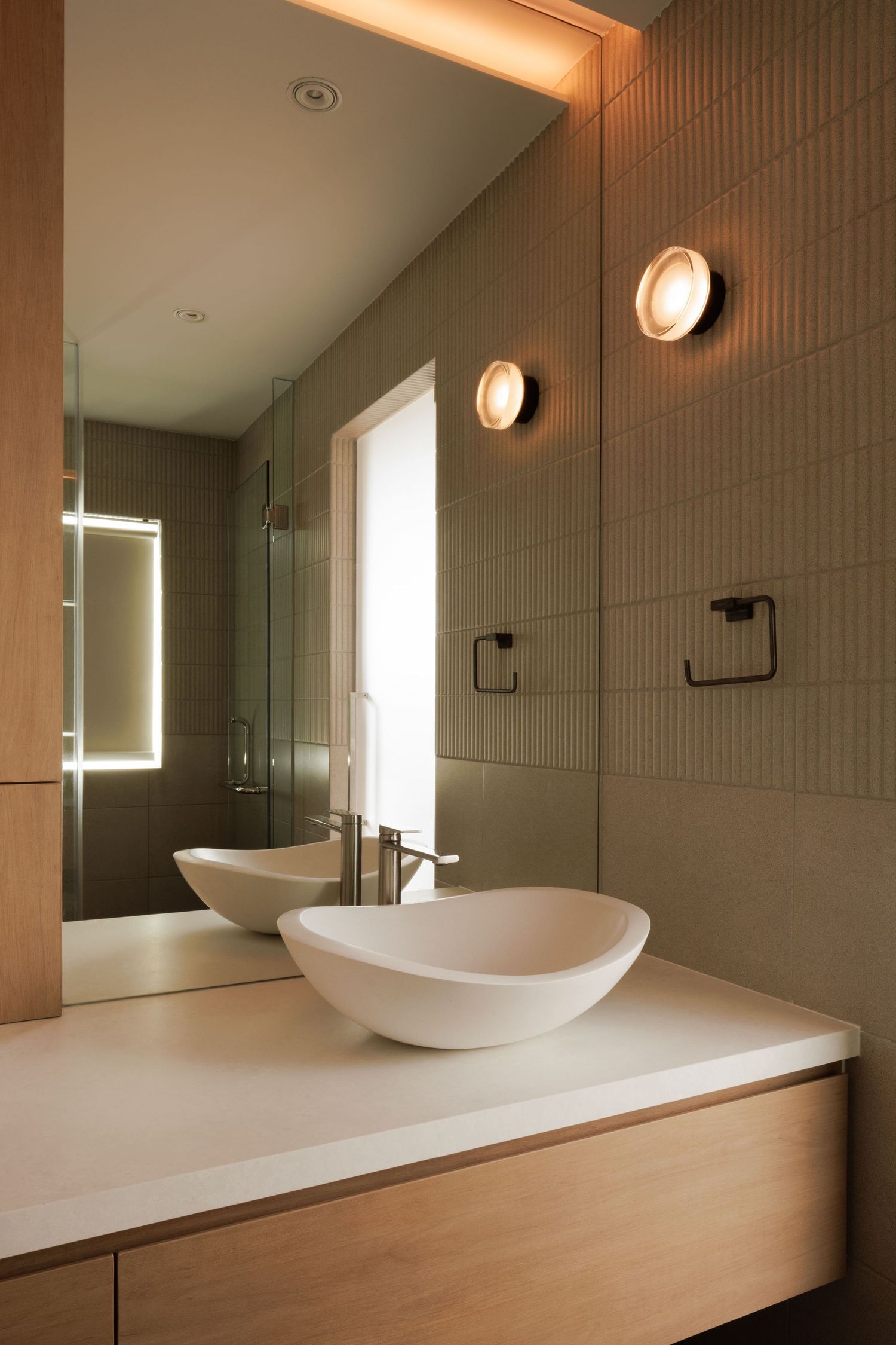 Modern bathroom interior with sleek vessel sink on wooden vanity and vertical lighting fixtures mounted on textured wall.