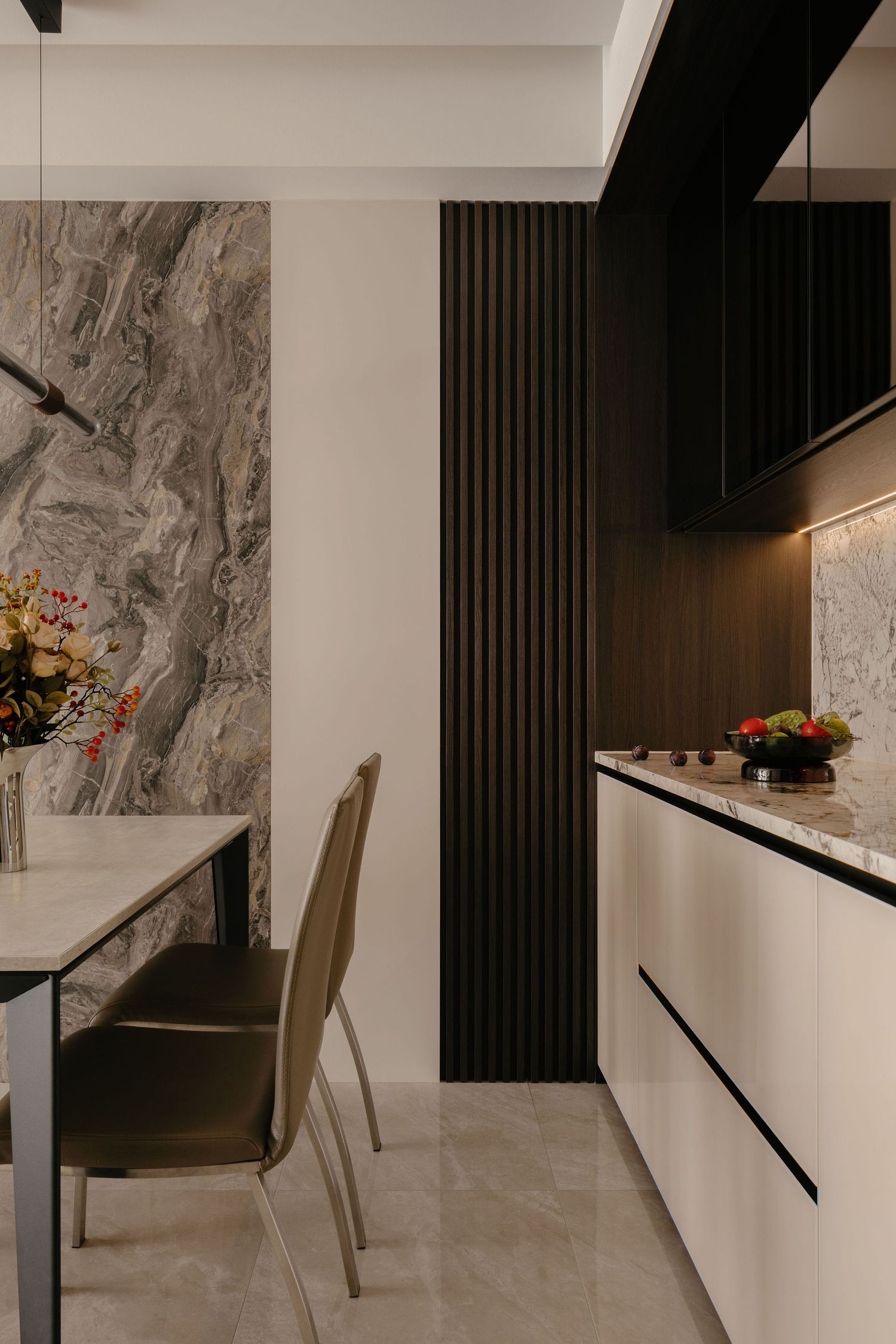Modern dining area with gray marble feature wall, dark fluted wood paneling, cream cabinetry, leather chairs and a floral centerpiece.