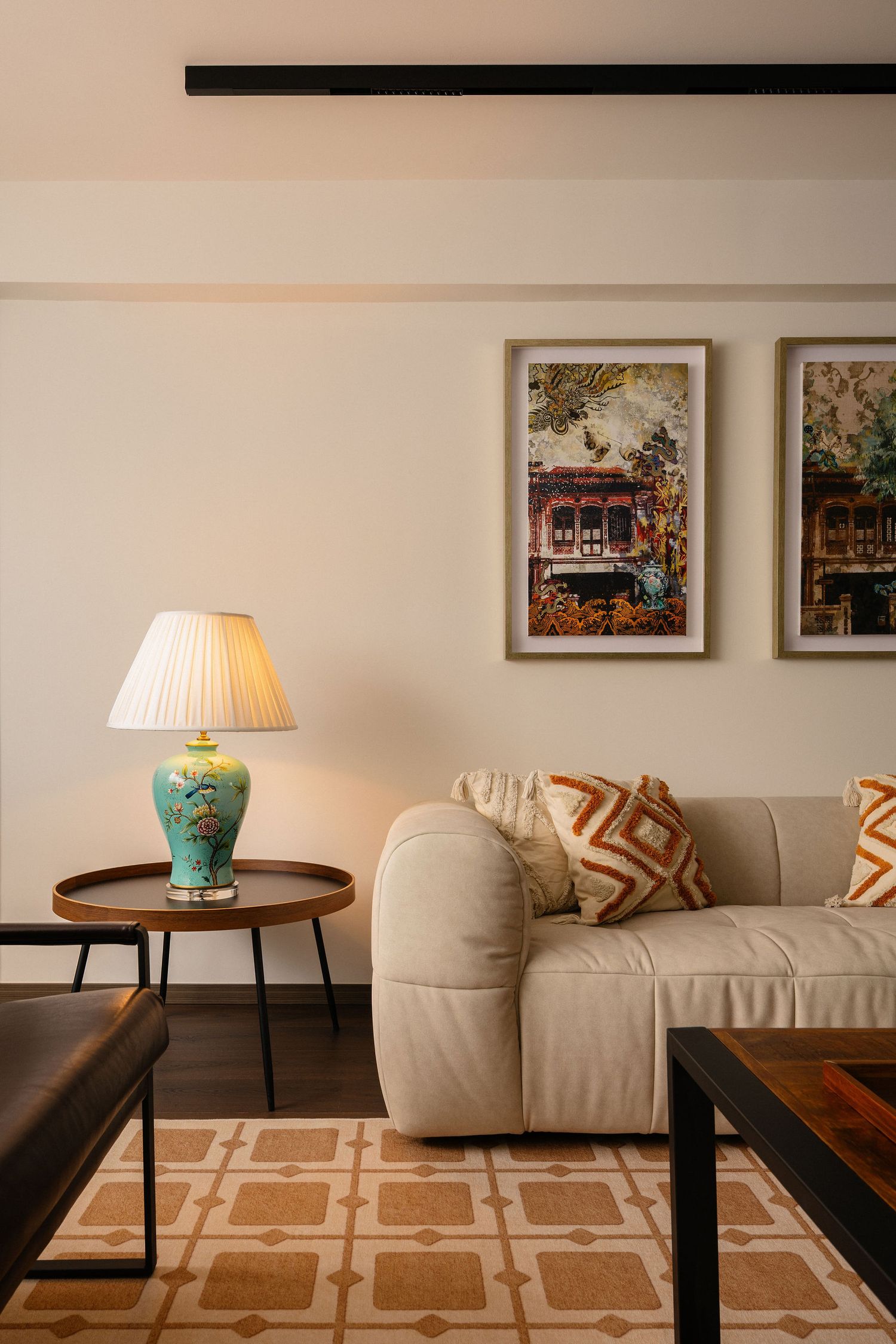 Cozy living room with beige sofa, orange geometric pillows, turquoise table lamp, patterned rug, and framed artwork on wall.