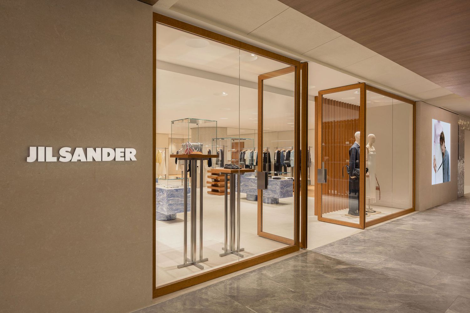 Jil Sander luxury fashion boutique storefront with warm wood frame displays and minimalist interior design.
