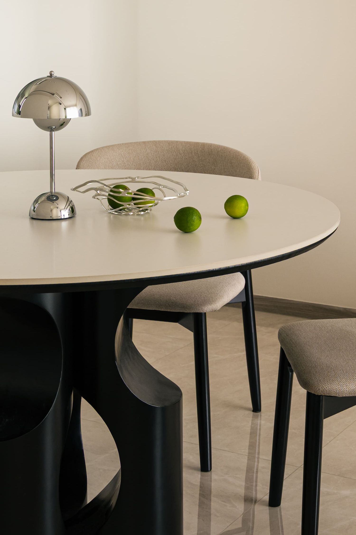 Modern dining table with chrome lamp, limes, and beige upholstered chairs on marble floor.