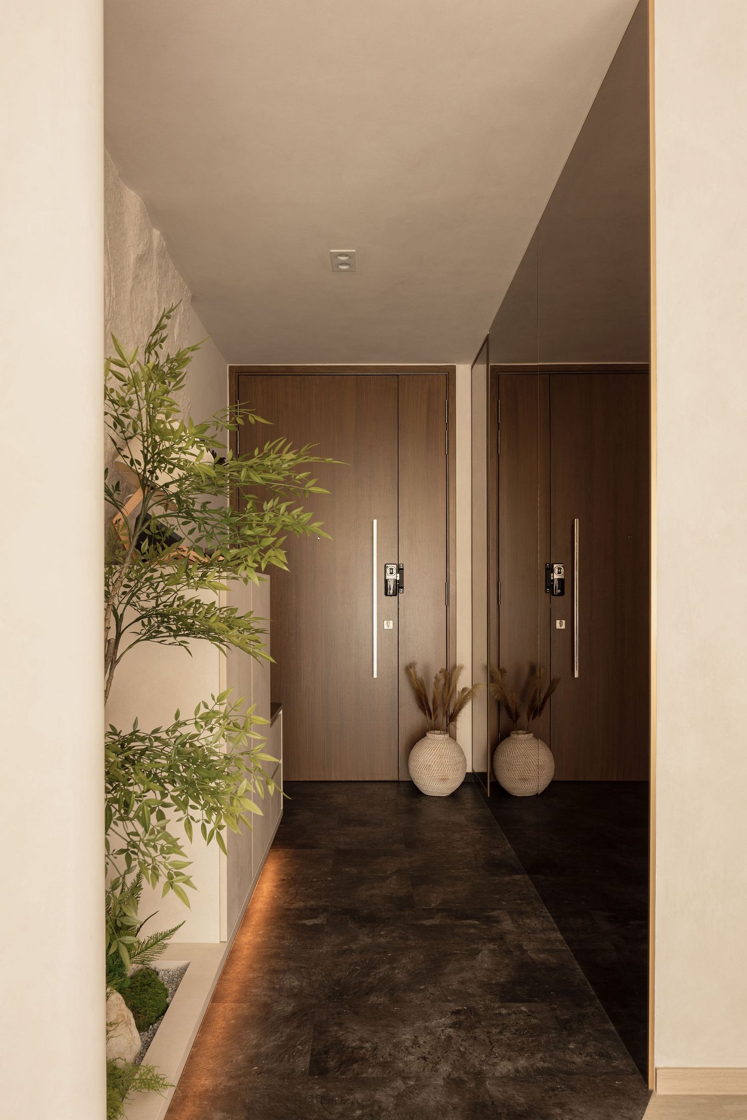 Modern hallway with dark stone floors, wooden doors, wall sconces, decorative vases, and lush green plants in warm lighting.