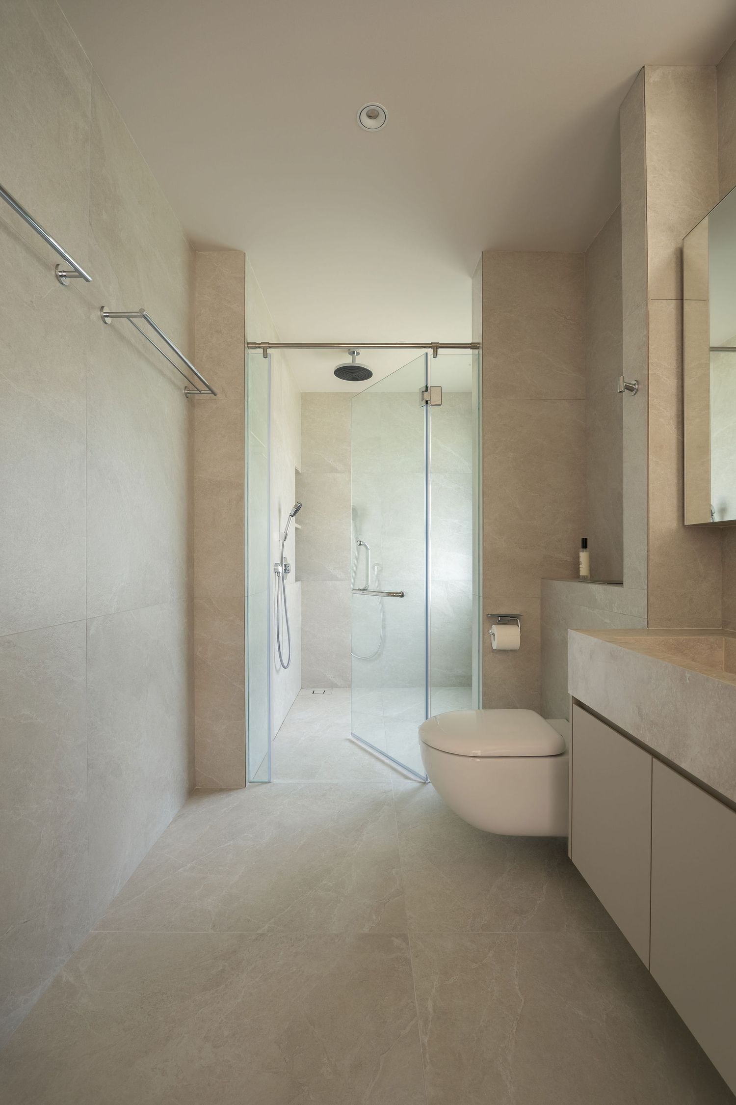 Modern minimalist bathroom with beige marble tiles, glass shower enclosure, wall-hung toilet, and floating vanity unit.