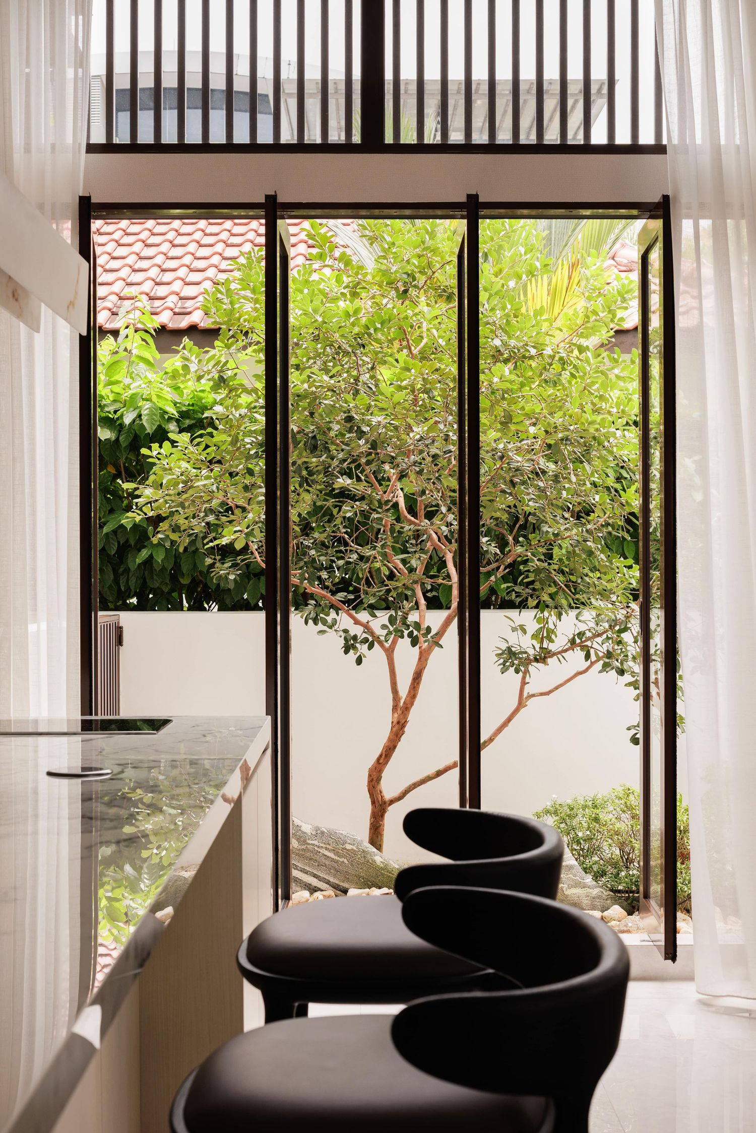 Modern office waiting area with black curved chairs and floor-to-ceiling windows overlooking a garden space.