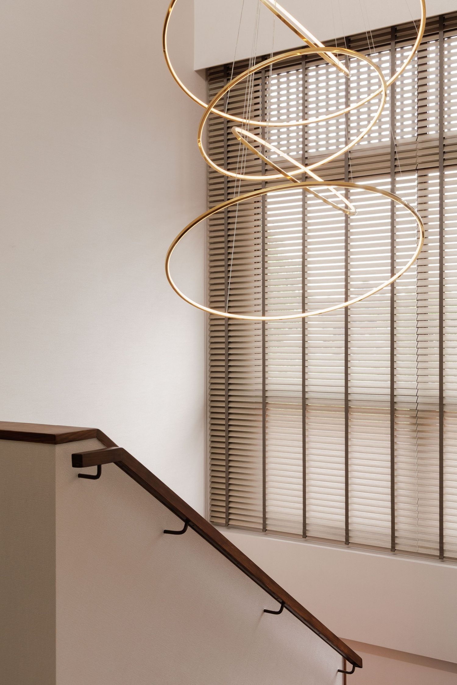 Modern minimalist hallway features white walls, dark wood handrail, and circular pendant light fixture with blinds on window.