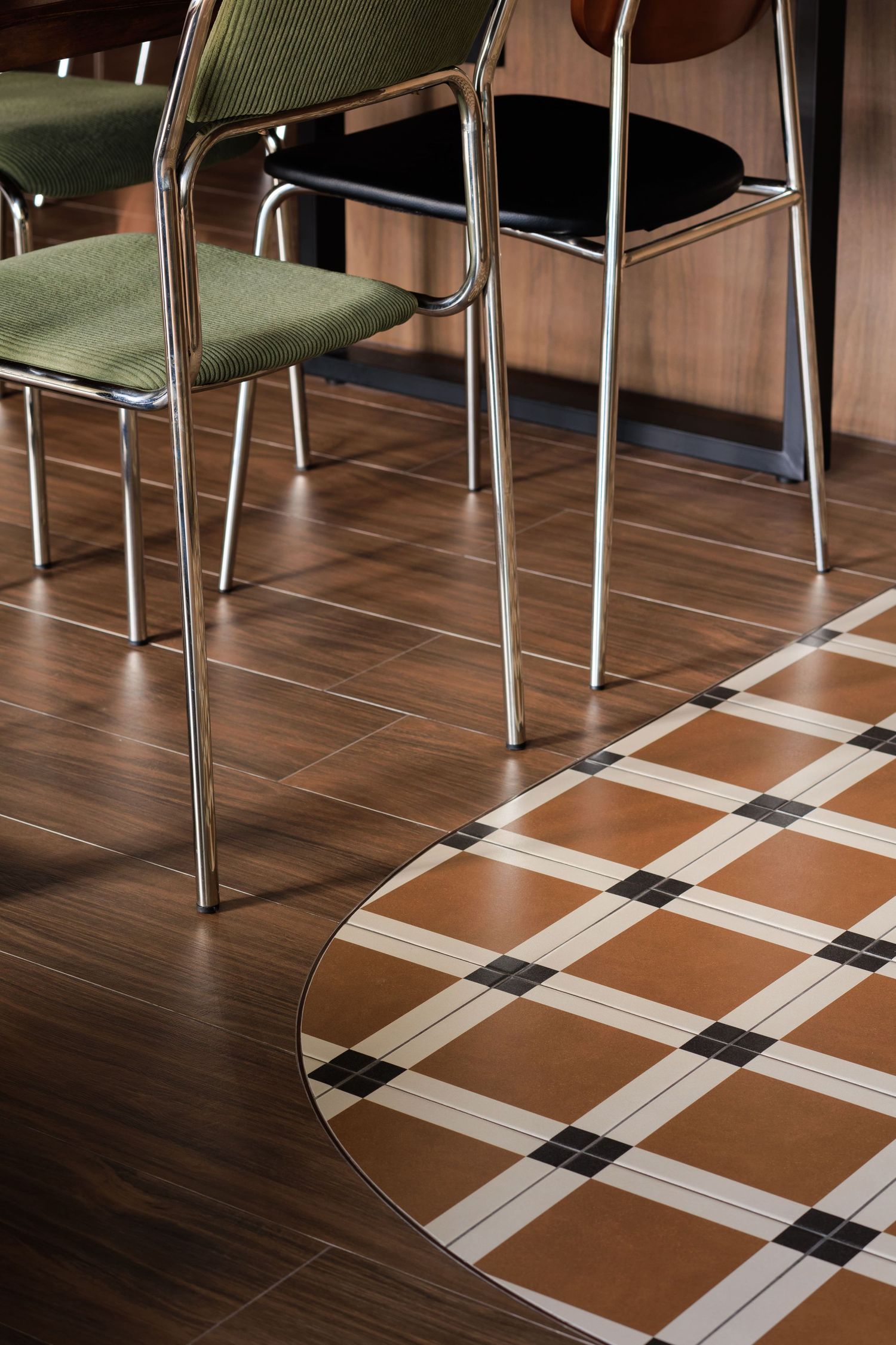 Modern dining area with green chairs, hardwood flooring and a geometric patterned round area rug in brown and white tones.