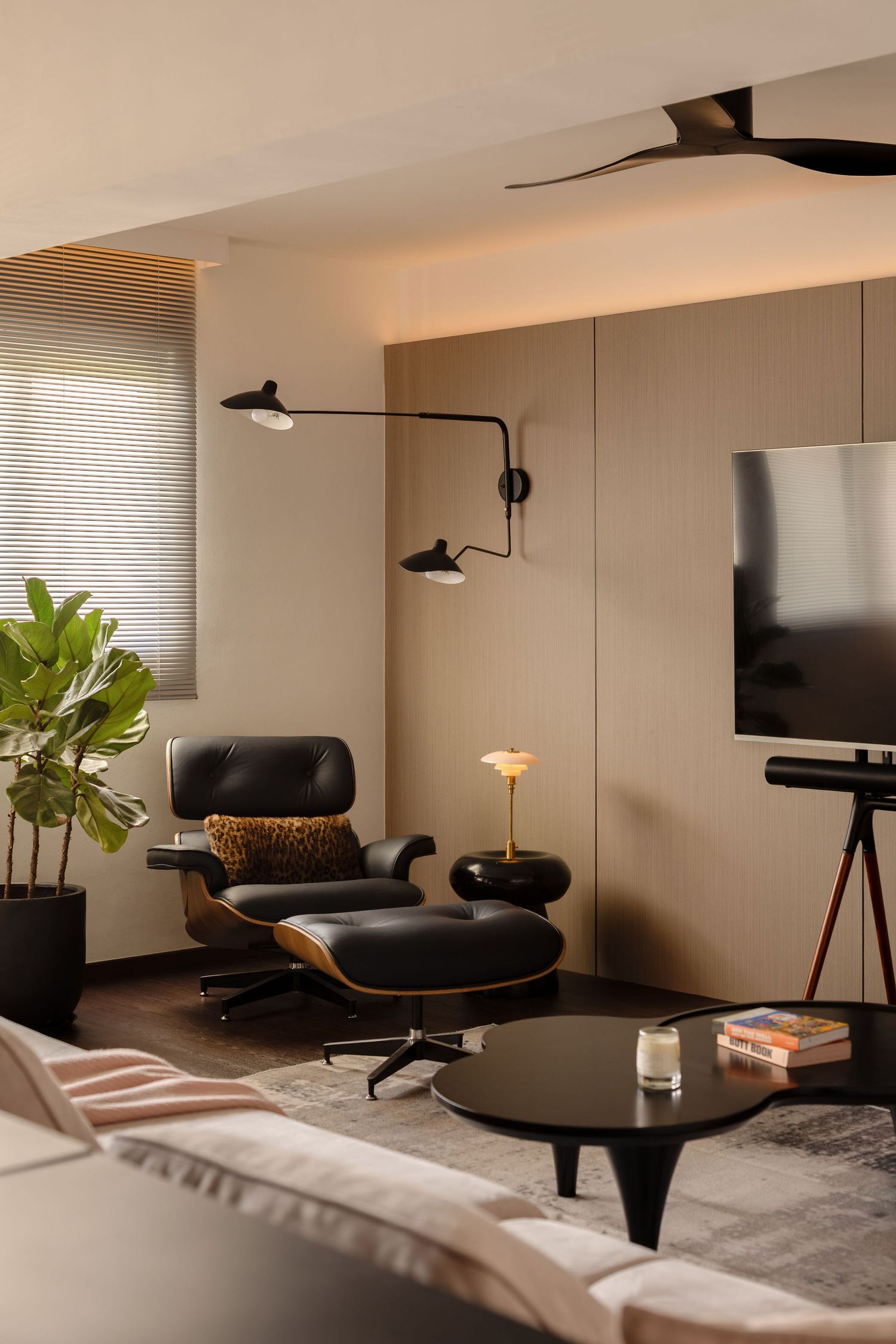 Modern living room with Eames lounge chair, black coffee table, wall-mounted TV, and stylish pendant lights in neutral tones.