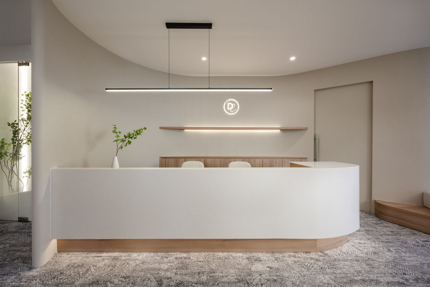 Modern minimalist office reception area with curved white desk, floating pendant light, and wooden accent wall.