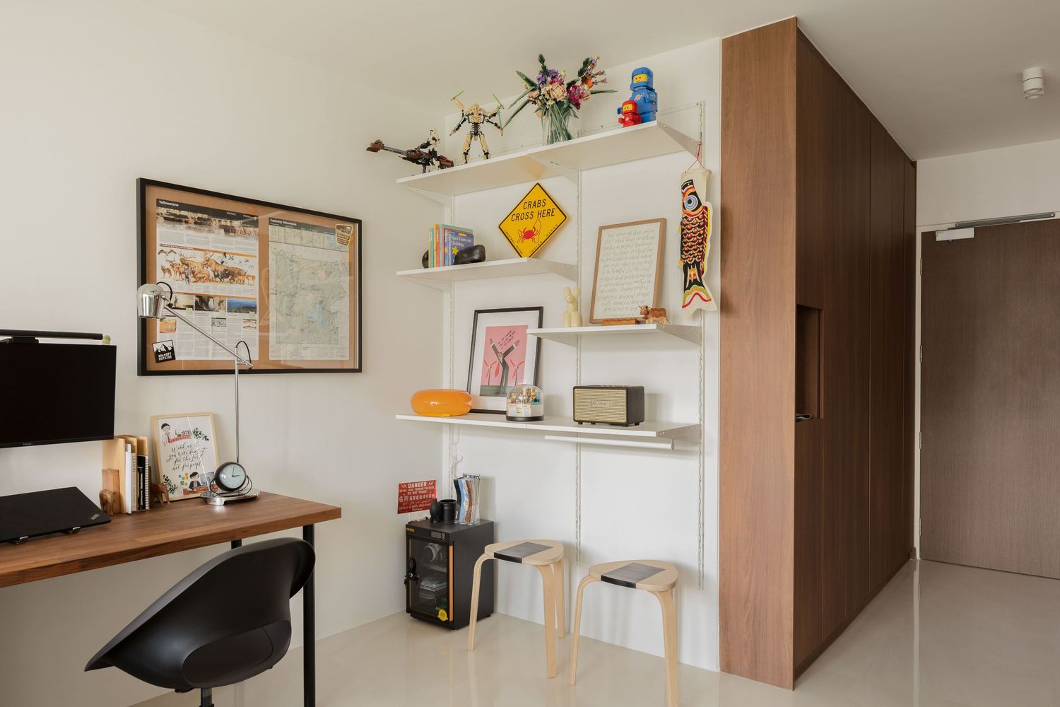 Modern home office with wooden desk, black chair, white shelving unit displaying decor, and warm wood wardrobe.