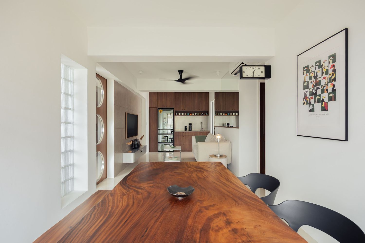 Modern open-plan dining room with a rich walnut wood table, dark chairs, and a view into a stylish kitchen with dark cabinetry.
