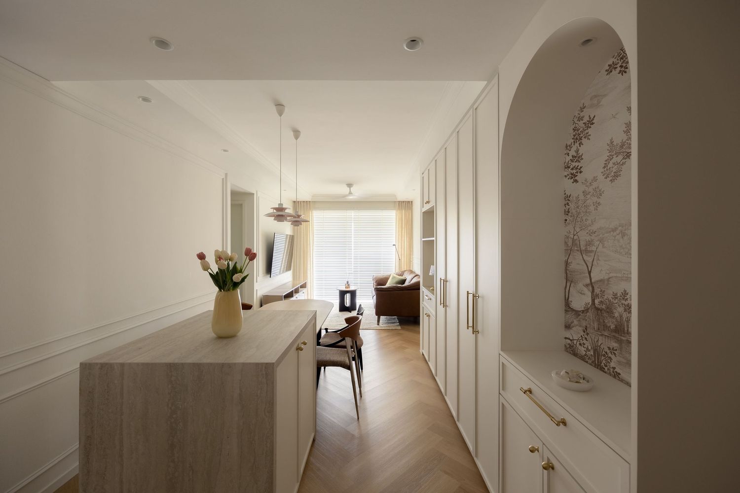 Modern open-plan living space with white cabinetry, arched alcove, herringbone floors, and neutral decor.